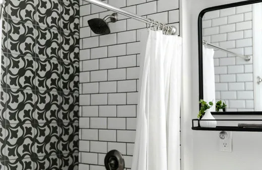 Black and white bathroom shower with white subway tiles and black grout lines, paired with patterned black tile accent wall and chrome fixtures.