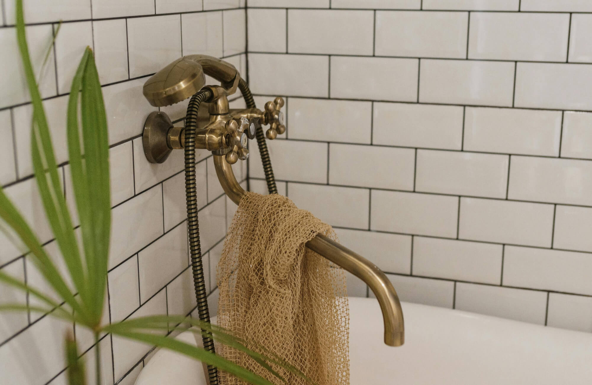 Vintage brass tub faucet against white subway tile wall with black grout in bathroom, highlighting classic tile layout and warm metal fixtures.