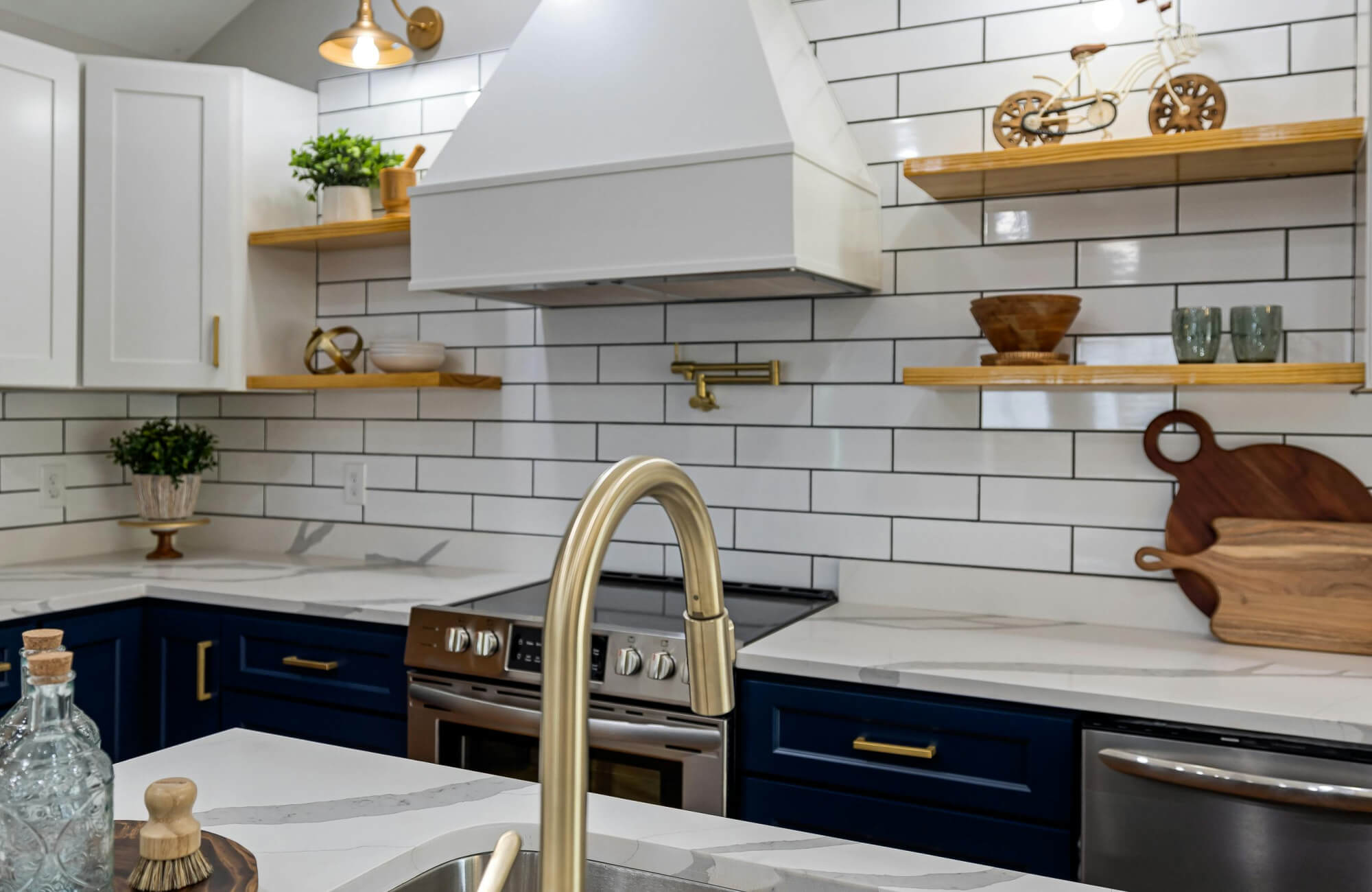 Bright kitchen with white subway tile backsplash and black grout, complemented by wood shelves, brass fixtures, and navy cabinetry.