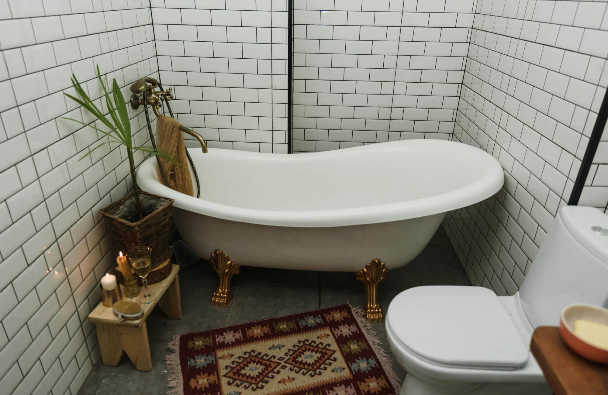 Freestanding bathtub with brass claw feet beside white subway tile walls and black grout in cozy bathroom with vintage-inspired décor.