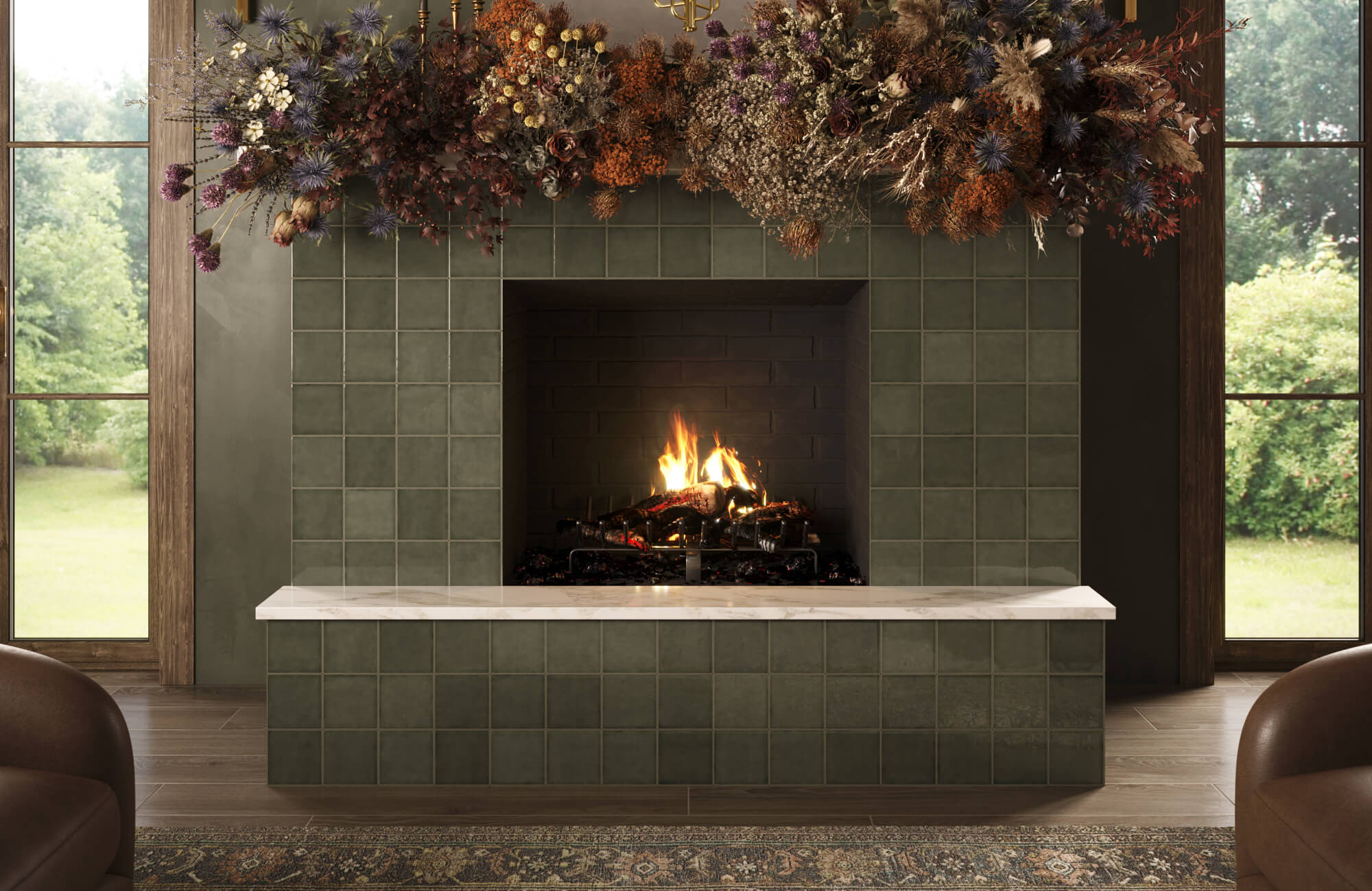 Cozy living room fireplace with green zellige-style tile surround, marble hearth, glowing fire, dramatic dried floral mantel arrangement, and garden views.