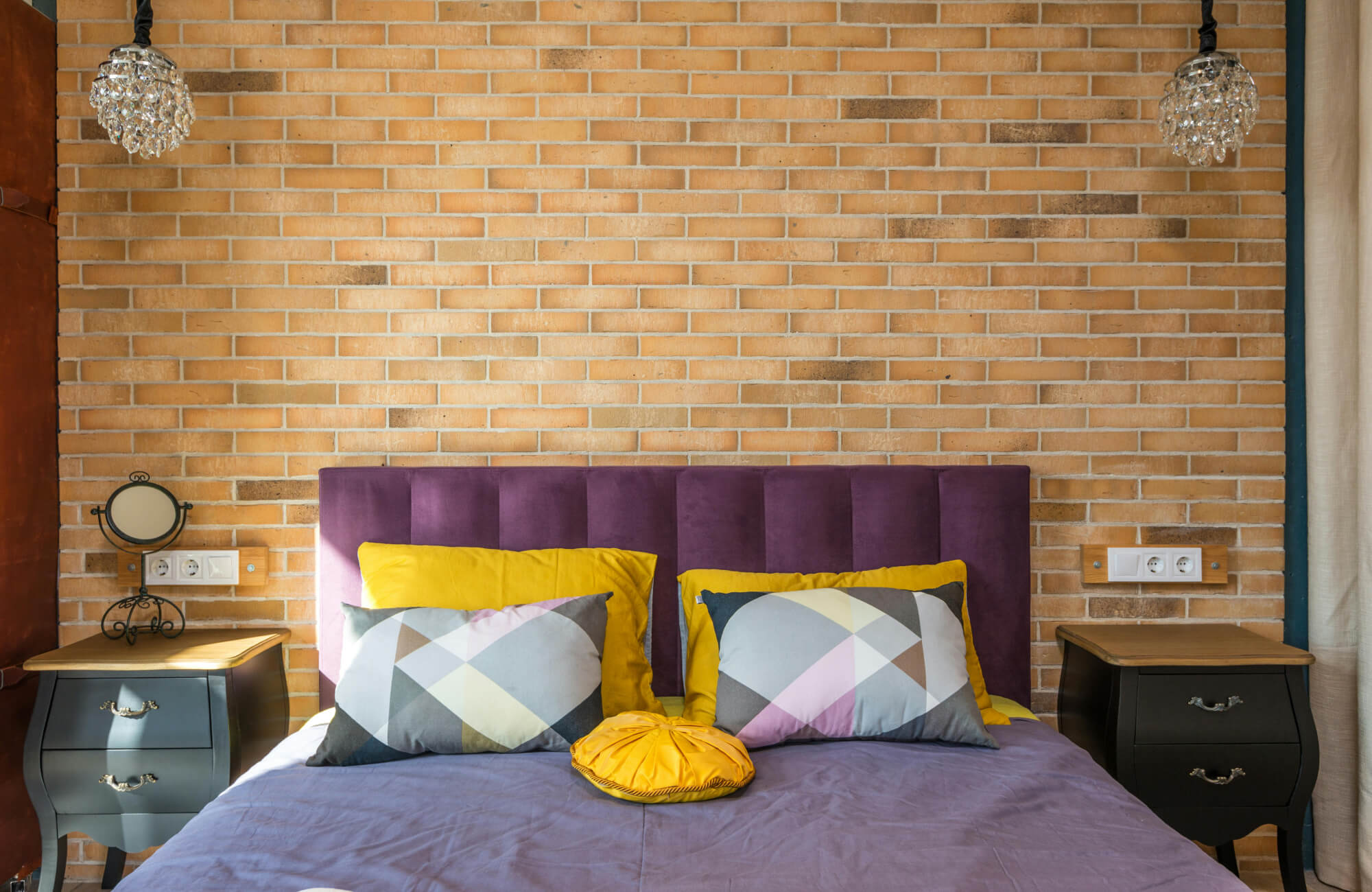 Cozy bedroom with a zellige-style tile wall, upholstered purple headboard, patterned pillows, black nightstands, and decorative pendant lights.