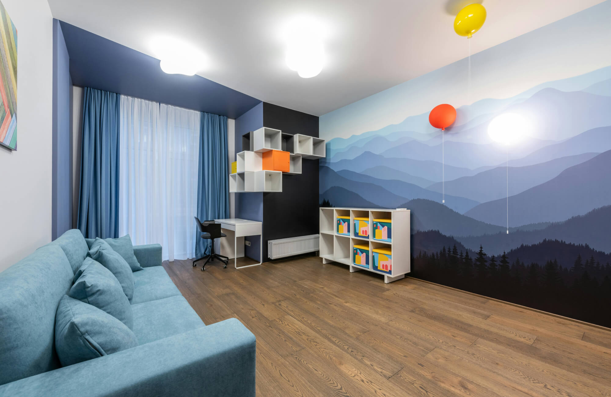 Modern kids’ room with blue mountain mural wallpaper, warm brown wood look flooring, light blue sofa, and colorful floating cube shelves.