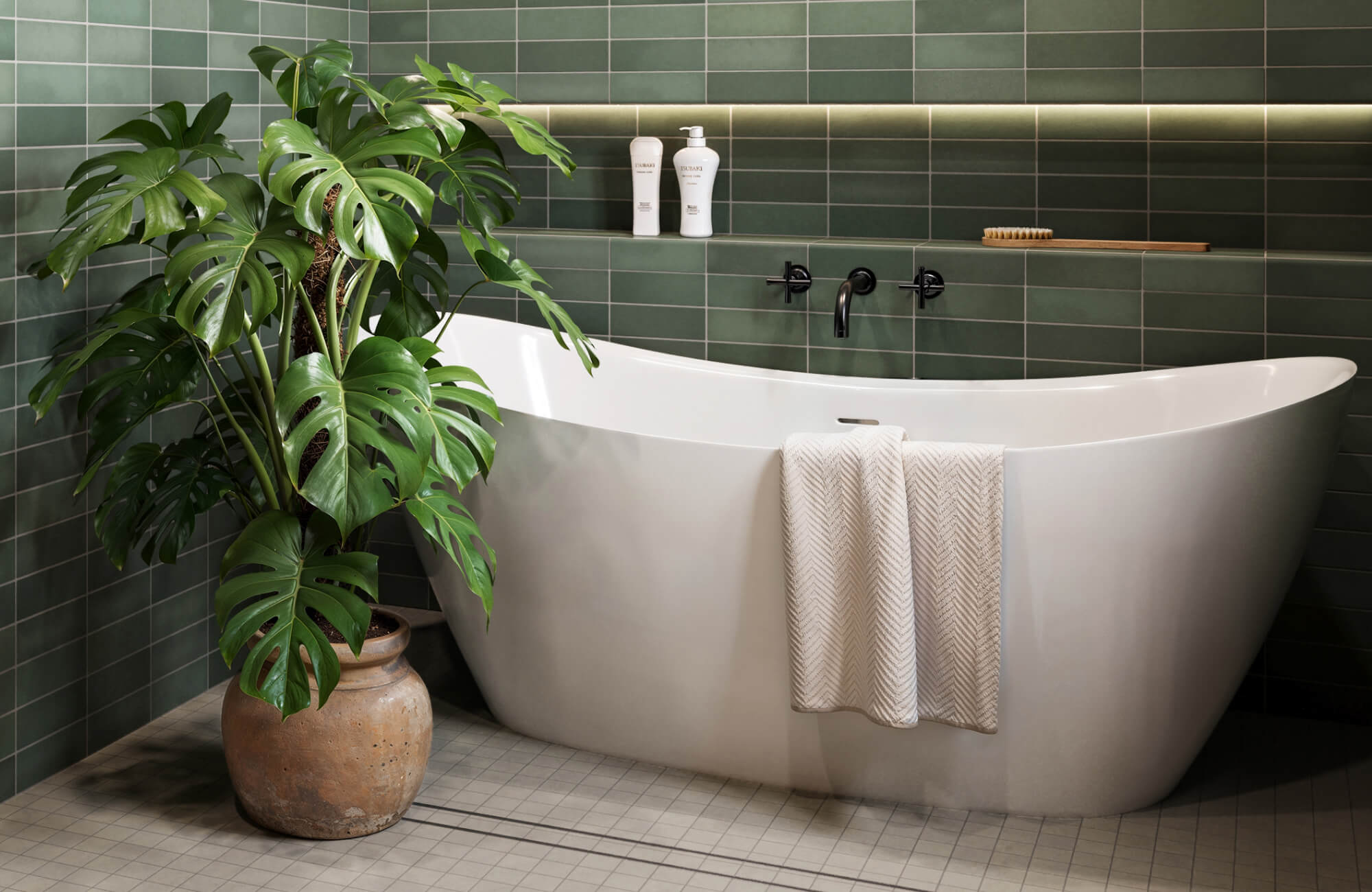 A serene bathroom featurig a freestanding soaking tub set against deep green tiled walls, accented by matte black fixtures, a built-in shelf with bath essentials, and a lush potted plant that adds a spa-like atmosphere to the bathroom.