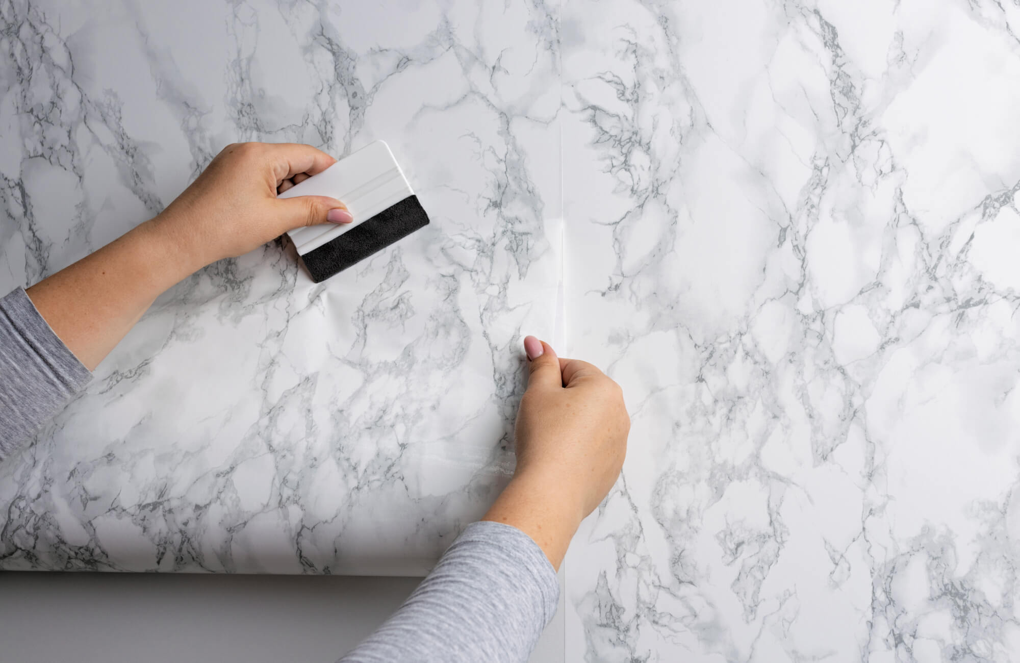 A diy bathroom remodel in progress shows hands carefully applying marble-look stick-on with a smoothing tool, highlighting a budget-friendly, hands-on approach to updating the bathroom with a clean, modern finish.
