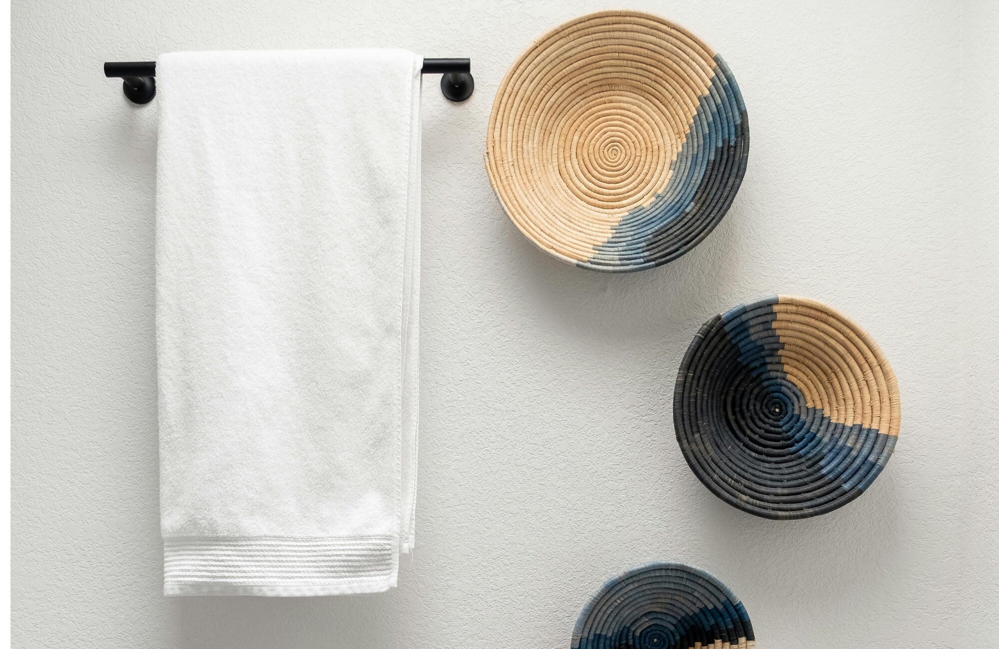A bathroom highlighting a clean white towel on a matte black bar alongside woven wall baskets, adding simple texture and handcrafted charm to a calm, minimalist bathroom space.