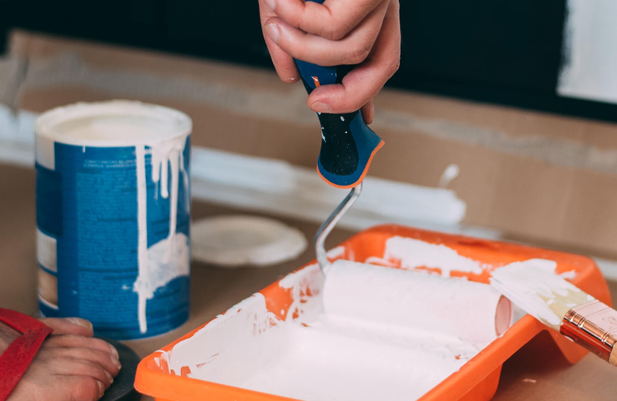 A diy bathroom remodel in progress captures hands loading a small paint roller with white paint from a tray, emphasizing the hands-on preparation and finishing work involved in refreshing the bathroom space.