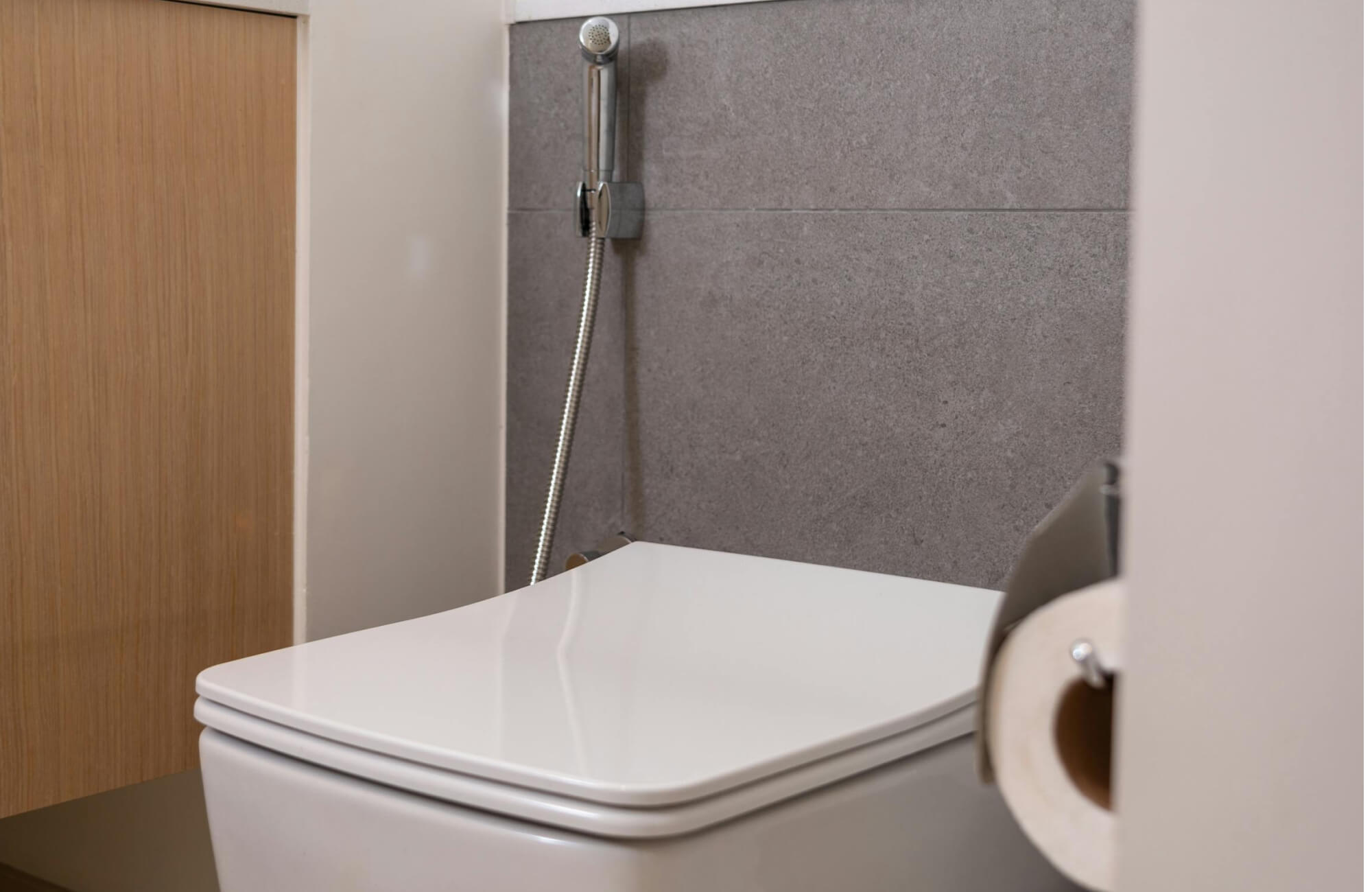 A bathroom showing a compact, modern toilet with a bidet, set against textured gray wall panels and warm wood accents for a clean, contemporary bathroom look.