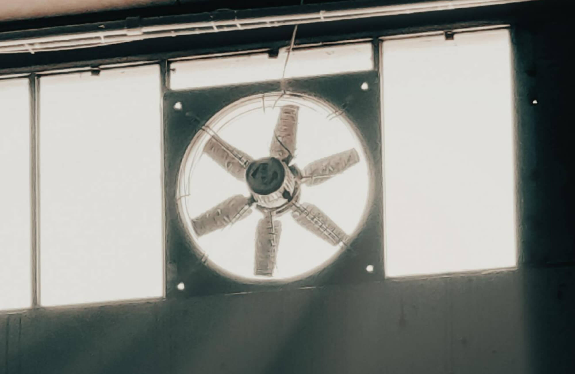 A bathroom with an industrial-style ventilation fan set within a high window, allowing natural light and airflow to improve function and comfort.