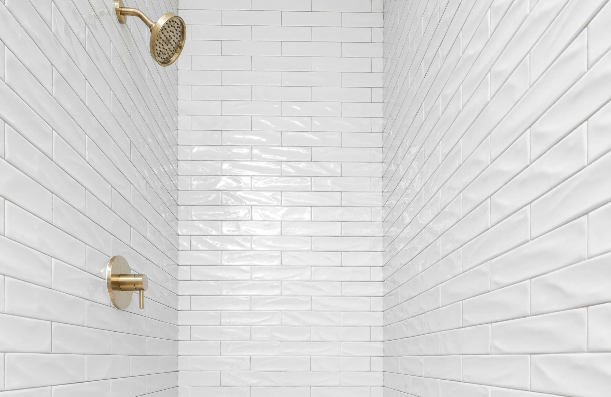 null Shower with glossy white subway tiles and brass fixtures against a clean, minimalist backdrop.