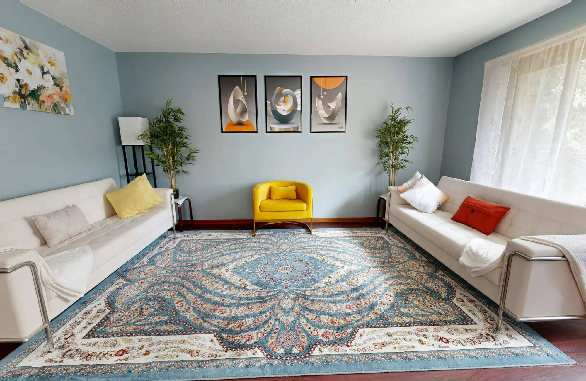 Bright living room with blue patterned rug, white sofas, and colorful decorative pillows arranged symmetrically.