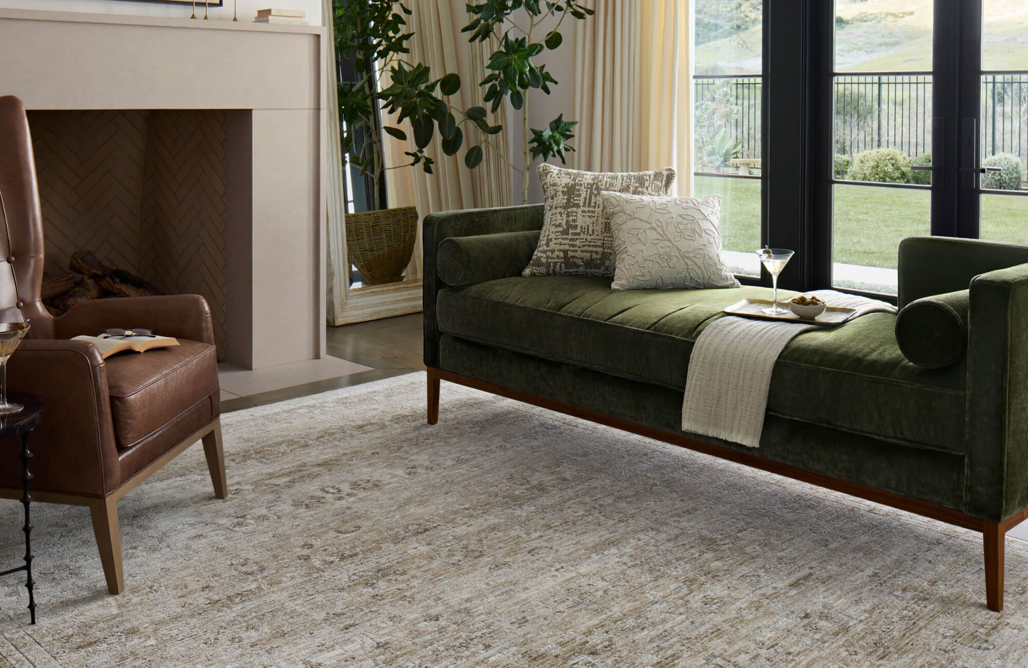 null Green velvet sofa with layered neutral pillows on a subtle textured rug in a light-filled modern living room.
