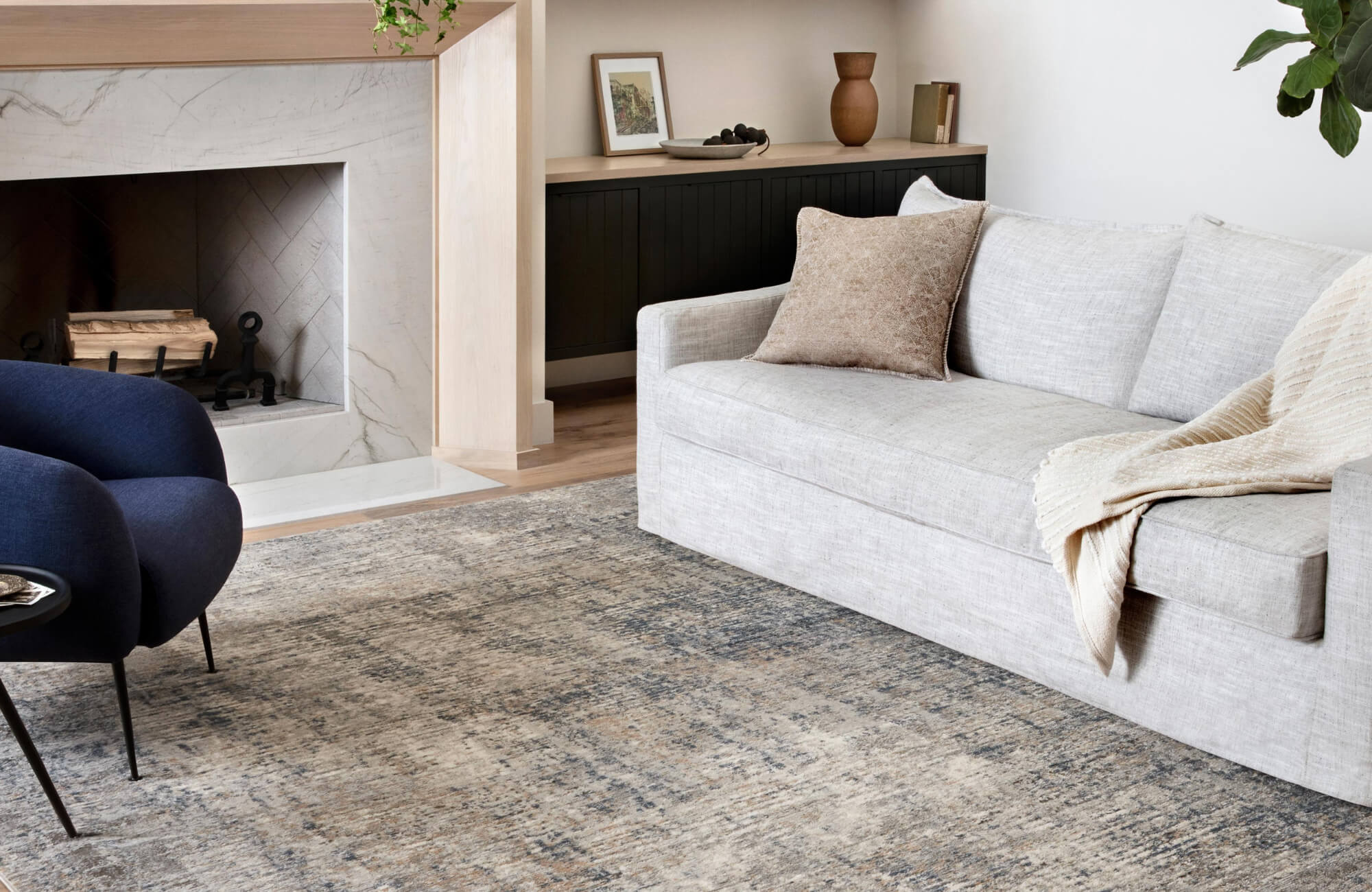 null Minimal living room with light gray sofa, warm-toned pillow, and distressed textured rug near fireplace.