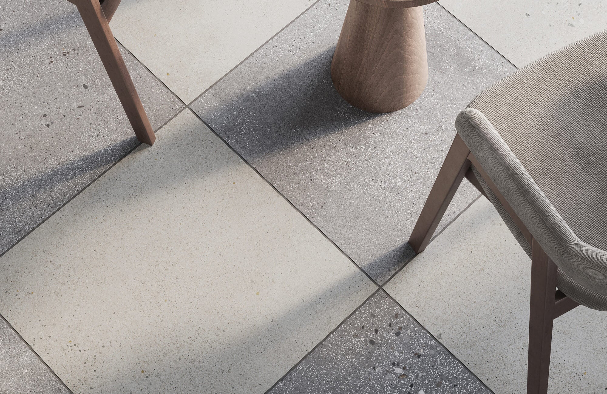 Close-up of a modern checkerboard floor featuring large, textured tiles in shades of light and dark gray, paired with wooden furniture