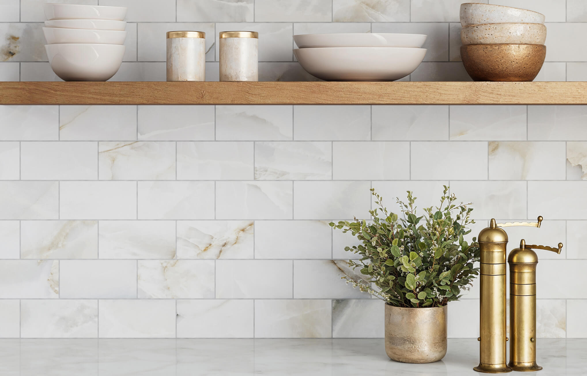 null White marble-look subway tiles in a running bond layout create an elegant kitchen backsplash styled with wood shelves and gold accents.