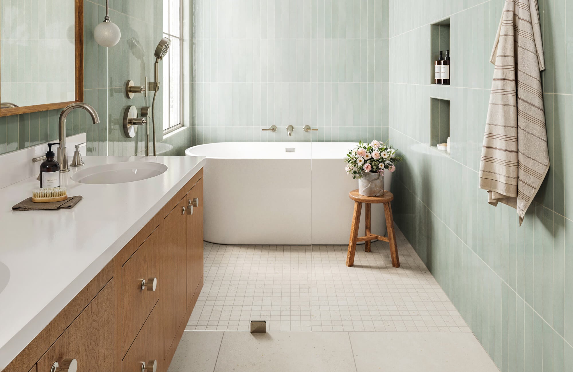 Bathroom with soft green vertical wall tile installation, small white mosaic floor tiles, and bathtub shower tile surround with built-in niches.