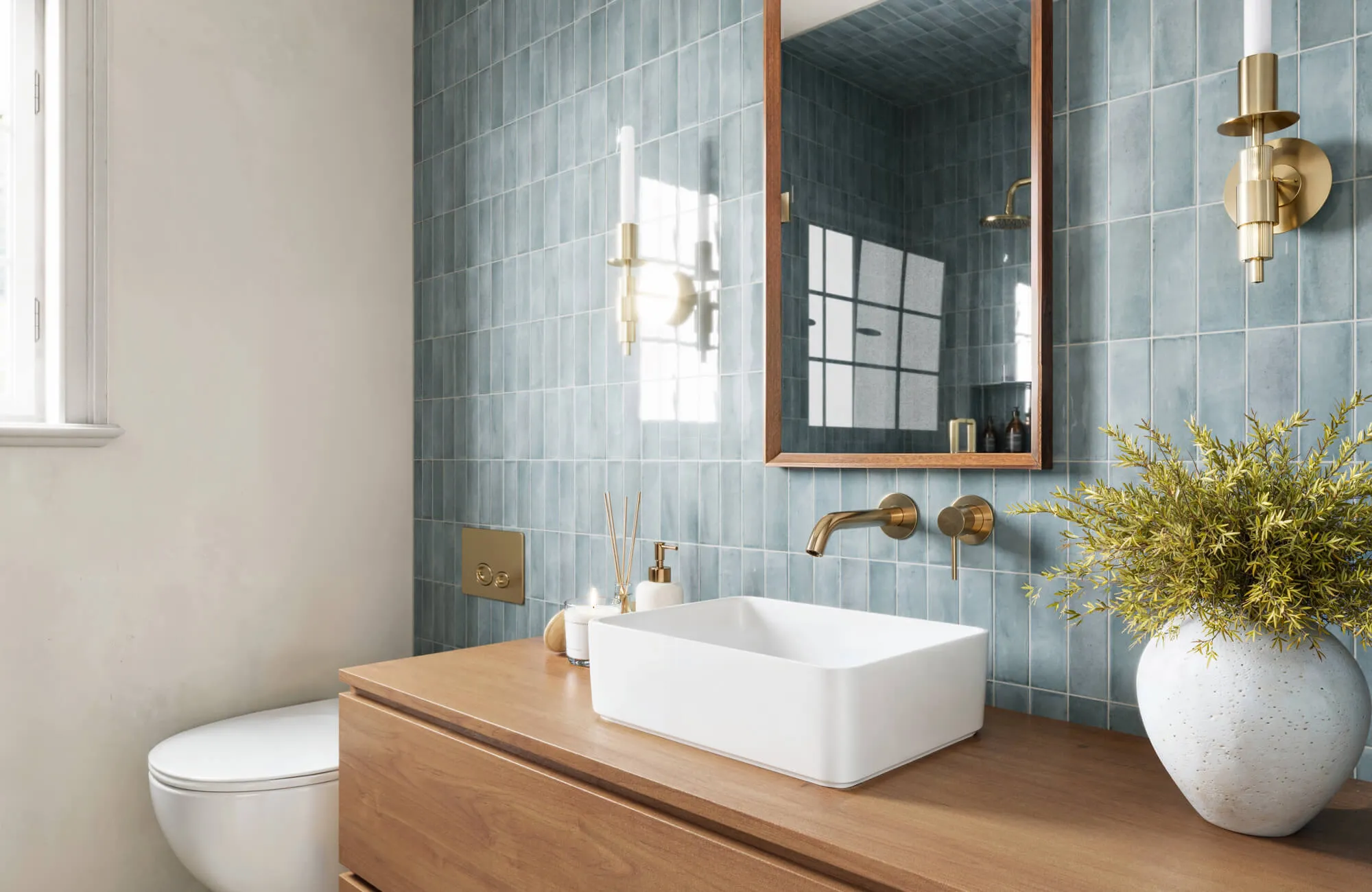 Blue vertical subway tile bathroom wall with brass fixtures, wood vanity, and square white vessel sink under framed mirror.