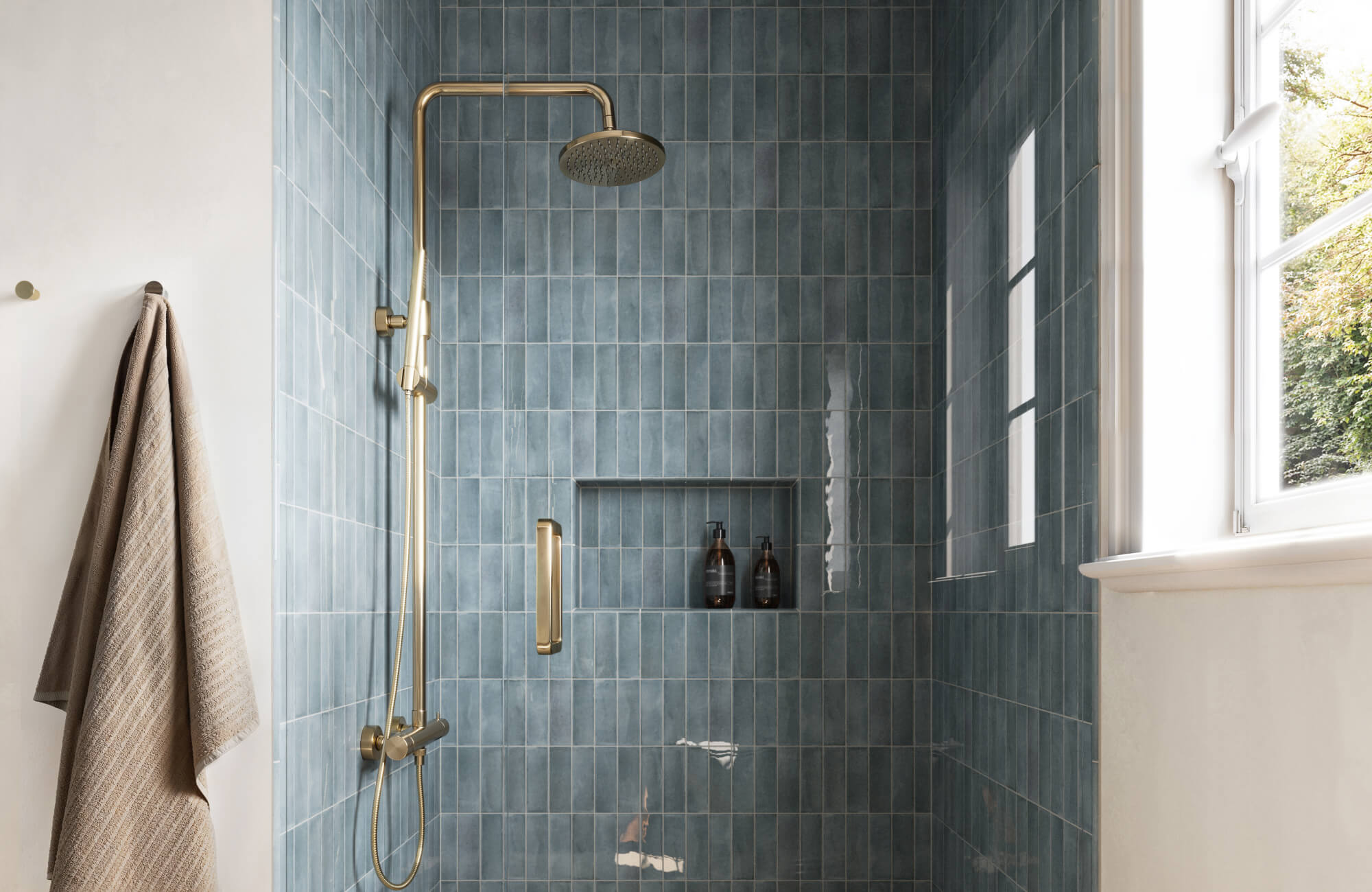 null Blue glossy subway tile shower walls in vertical stack layout with brass rainfall shower fixture and recessed niche.