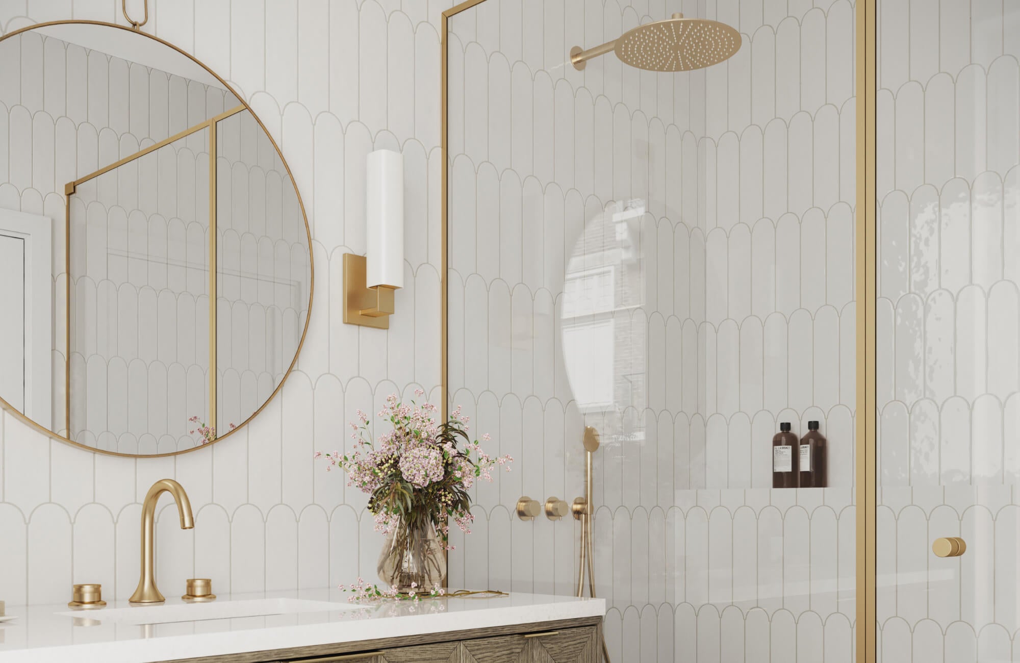 Elegant bathroom featuring white scalloped ceramic tiles, gold fixtures, a round mirror, and a walk-in shower with built-in niche shelving.