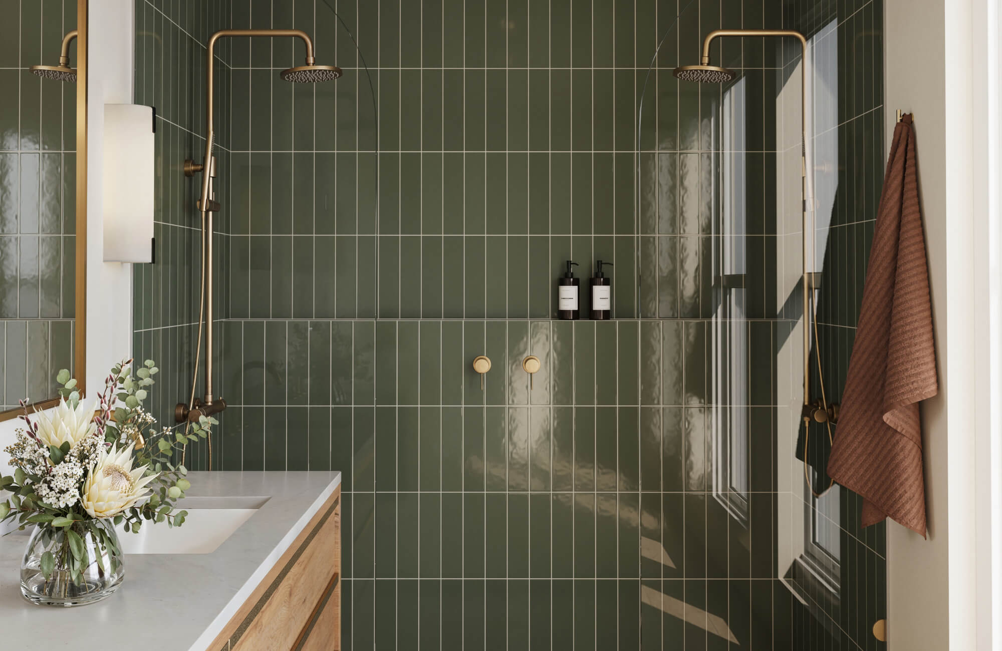Modern bathroom with glossy vertical green ceramic tiles, dual gold showerheads, a built-in niche, and a wood vanity with floral arrangement.