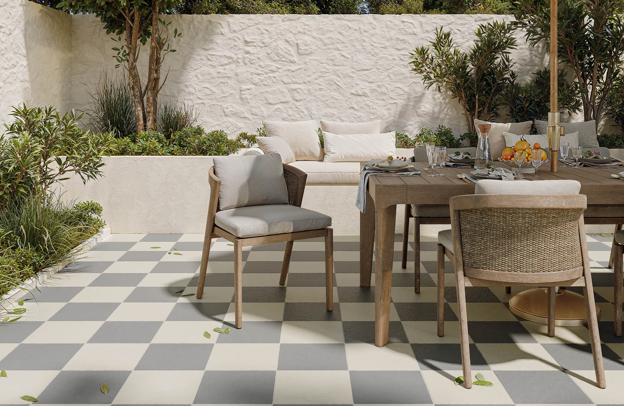 Cream and slate checkerboard tiles set the stage for a serene patio dining area with lush greenery and rustic wooden furniture.