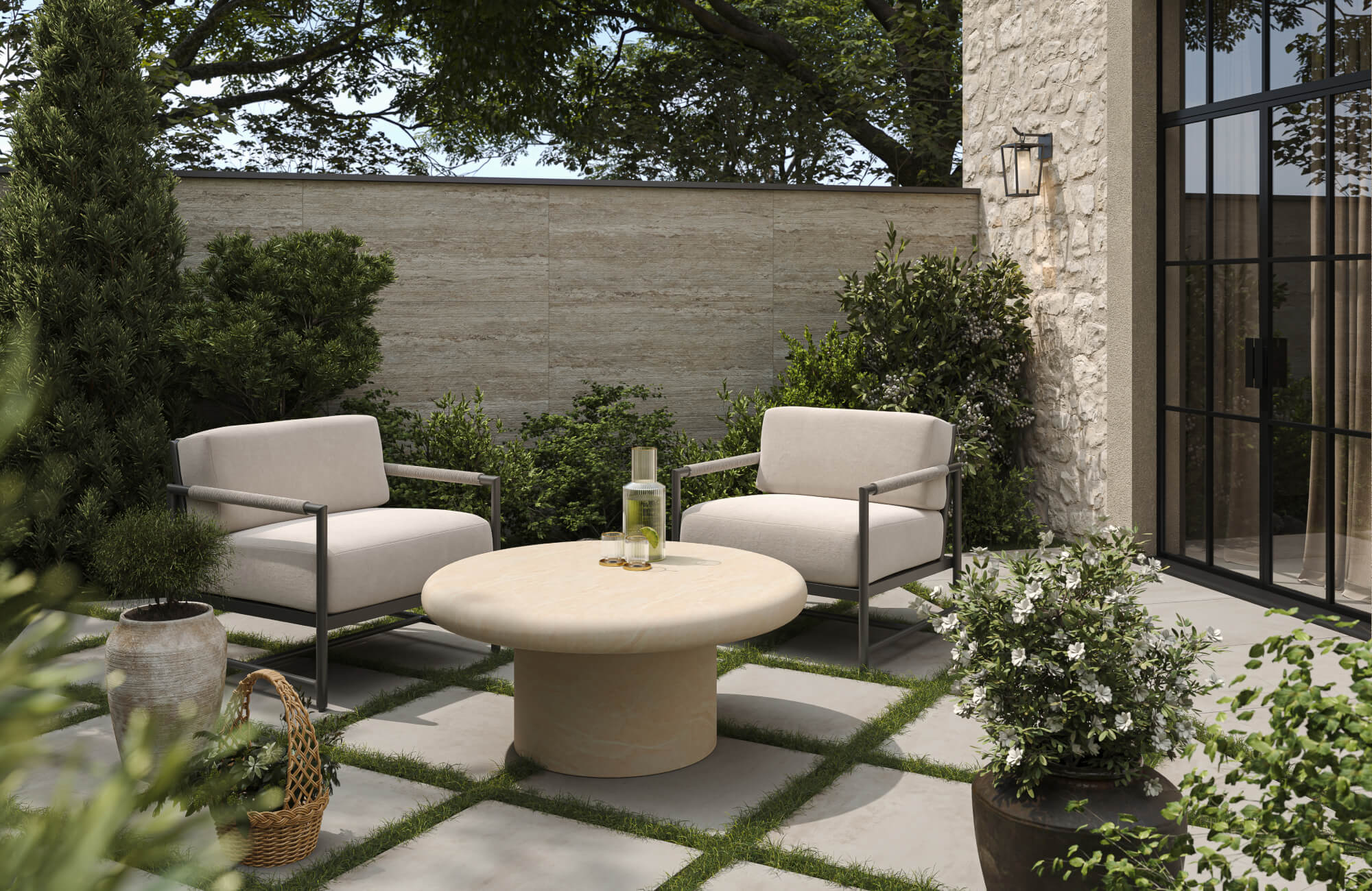 null In a garden patio, beige cushions sit on black metal chairs around a light beige table, surrounded by green plants and soft gray stone pavers.