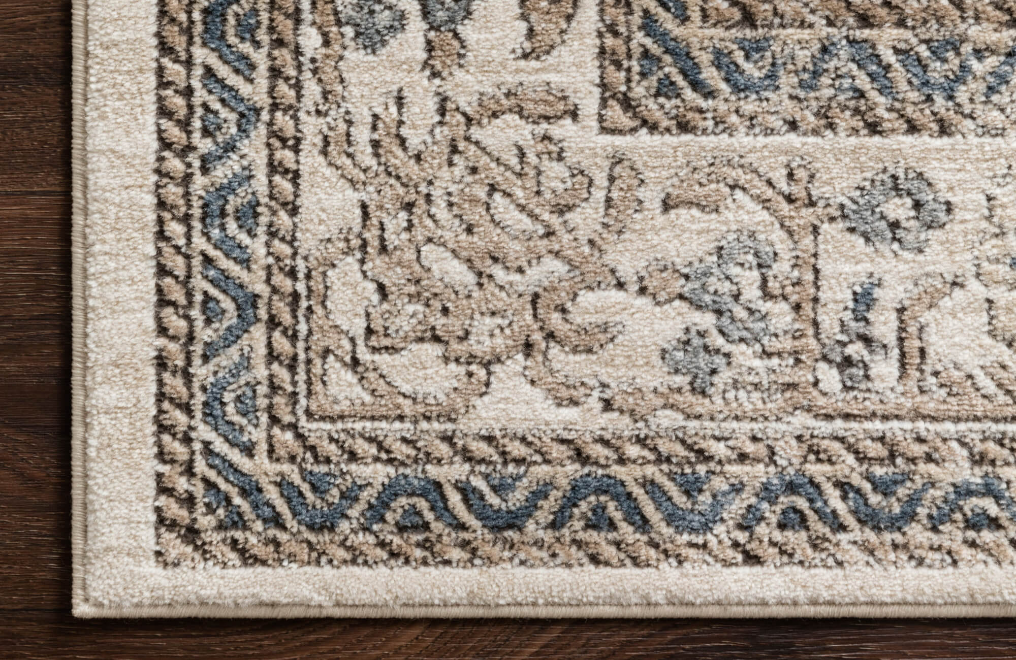 Detailed view of a patterned rug in soft beige with intricate brown and blue designs, styled over hardwood floors.