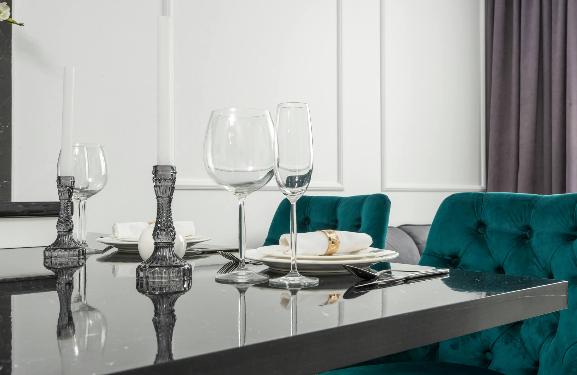 null A sophisticated dining area showcasing a polished glass dining table with reflective elegance, paired with plush teal velvet seating, minimalist table settings, and crystal accents for a refined, contemporary ambiance.