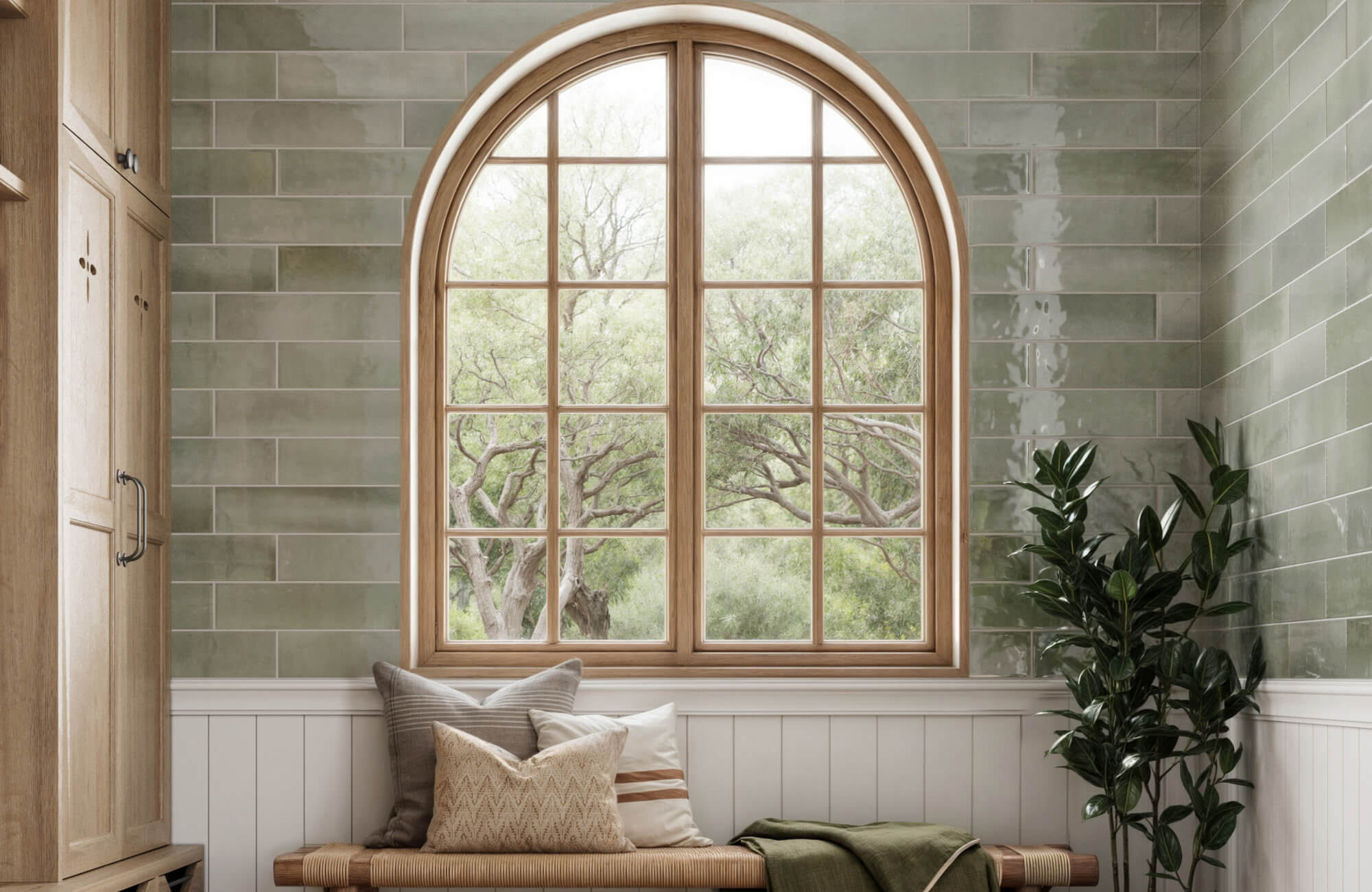 Sage green subway tiles and a wood-framed arched window create a calm, nature-inspired seating area with cozy pillows and soft daylight.