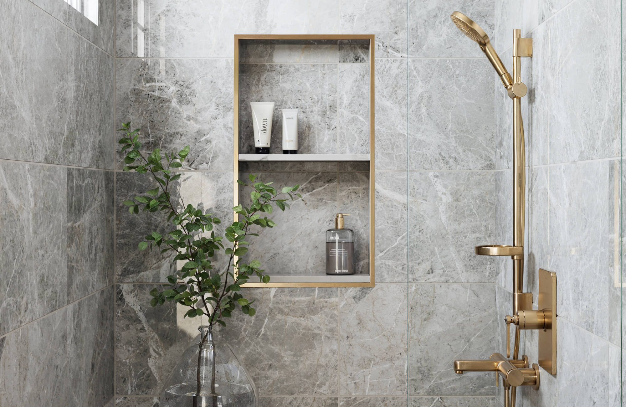 null Luxurious bathroom with marble look grey tiles, featuring a sleek gold shower fixture and built-in shelving, creating a refined, modern space.