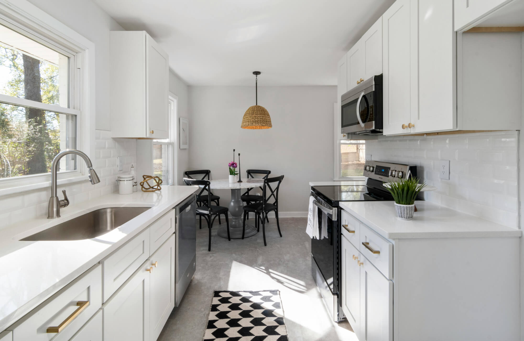 Modern white kitchen with brass hardware and a black-and-white geometric runner rug adding contrast to the light interior.