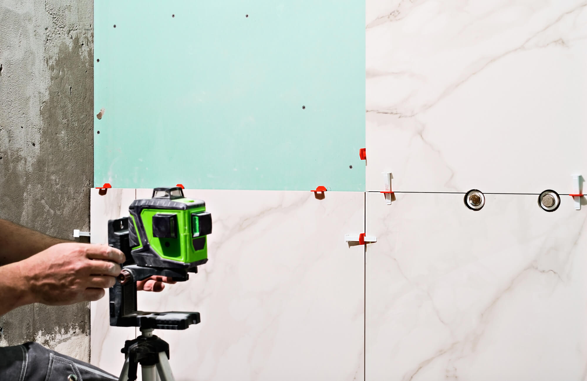 Large-format marble-look bathroom tiles are being installed with precision tools and spacers during wall application.