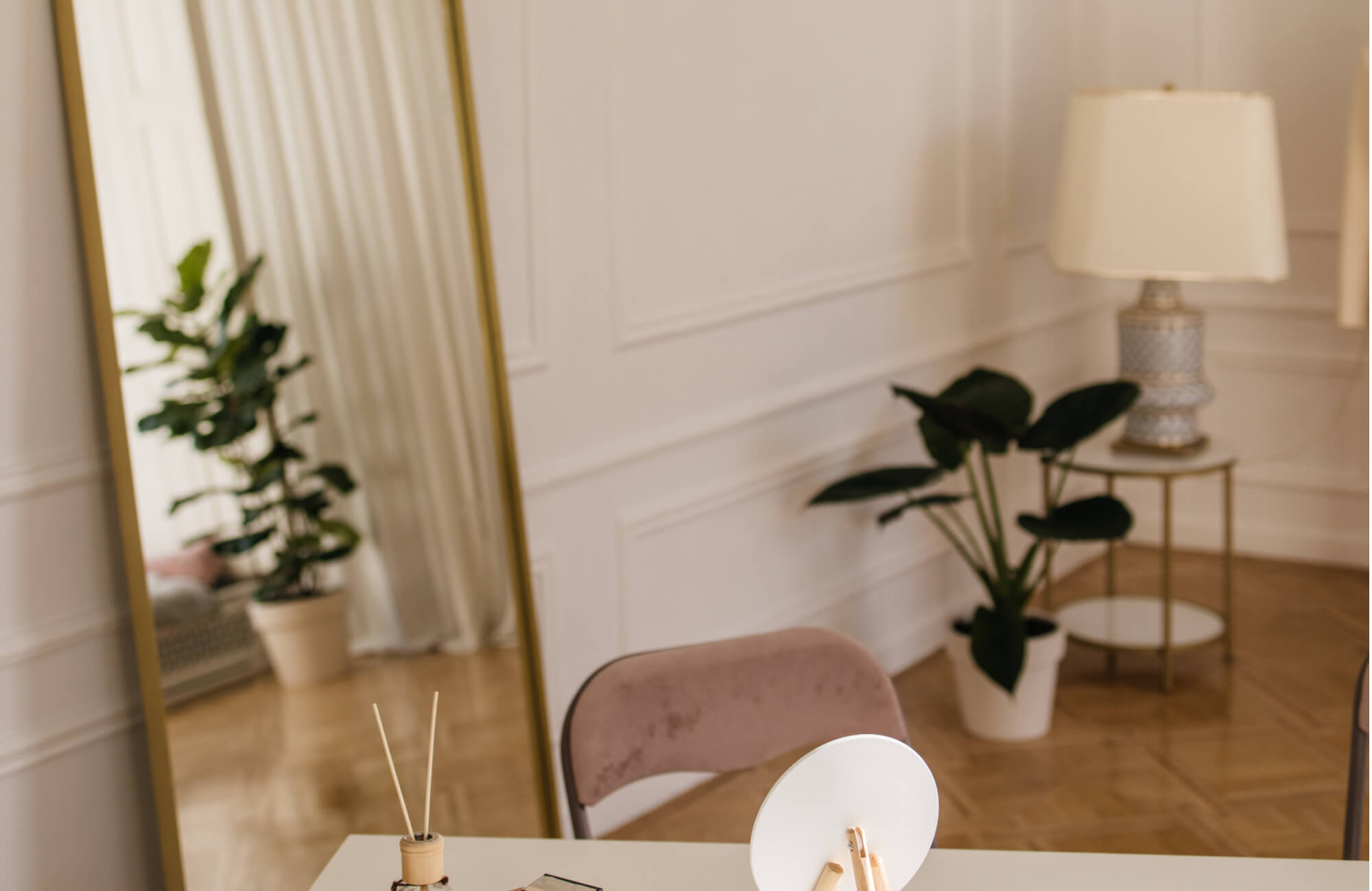null A bright, elegant room styled with soft neutrals features a large floor mirror with a sleek gold frame that reflects lush greenery and adds depth, warmth, and modern sophistication to the space.