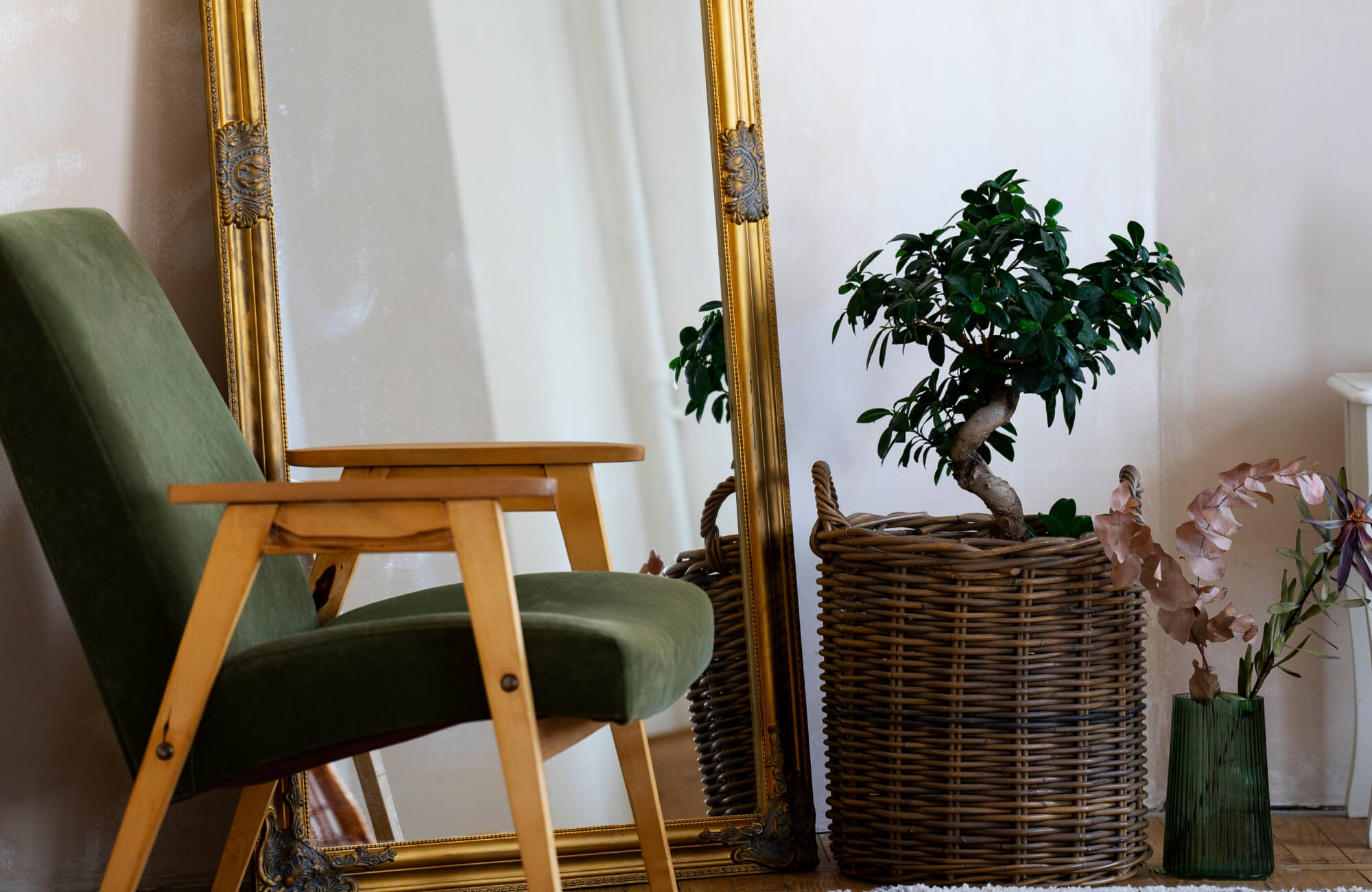 null A cozy, nature-inspired corner featuring a large floor mirror with an ornate gold frame, paired with a green mid-century chair, a woven basket planter, and soft botanical accents that create a warm, organic atmosphere.