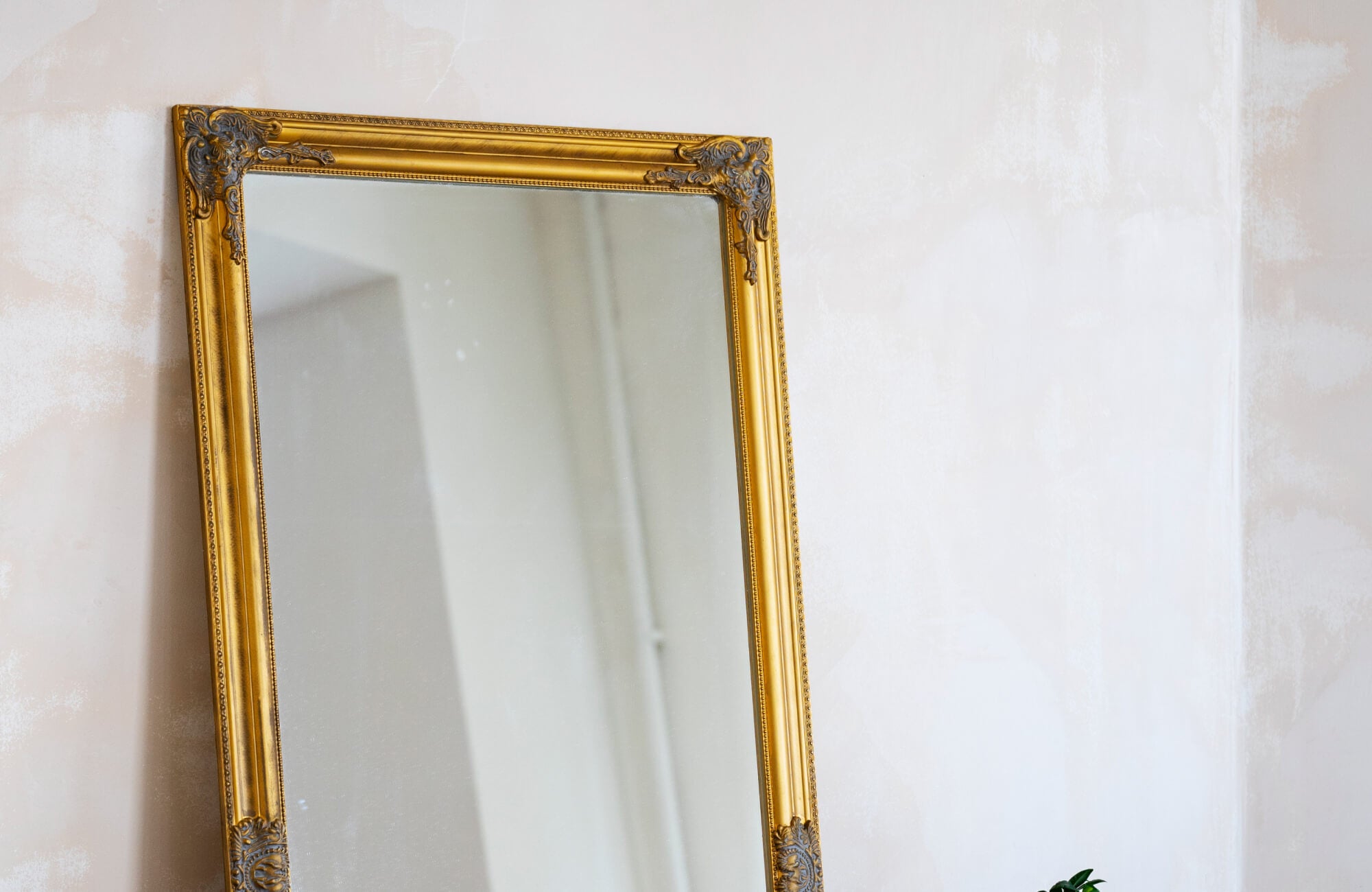 null A vintage-inspired interior showcasing a large floor mirror with an ornate gold frame, adding timeless elegance and reflective brightness to the softly textured wall backdrop.