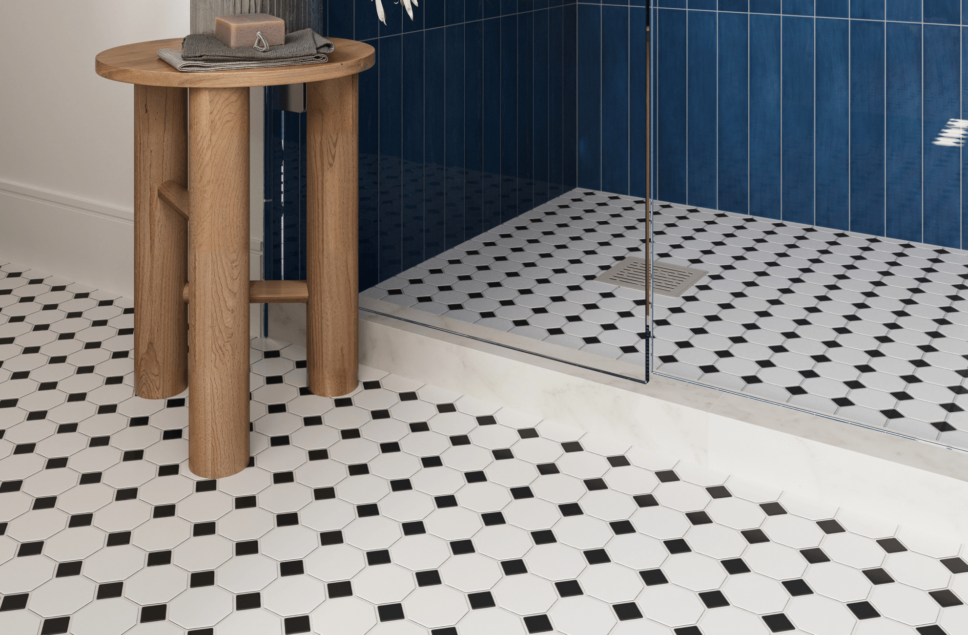 Classic white hexagonal tiles with black accents create a vintage-inspired floor design, paired with bold blue shower tiles and a rustic wooden stool.