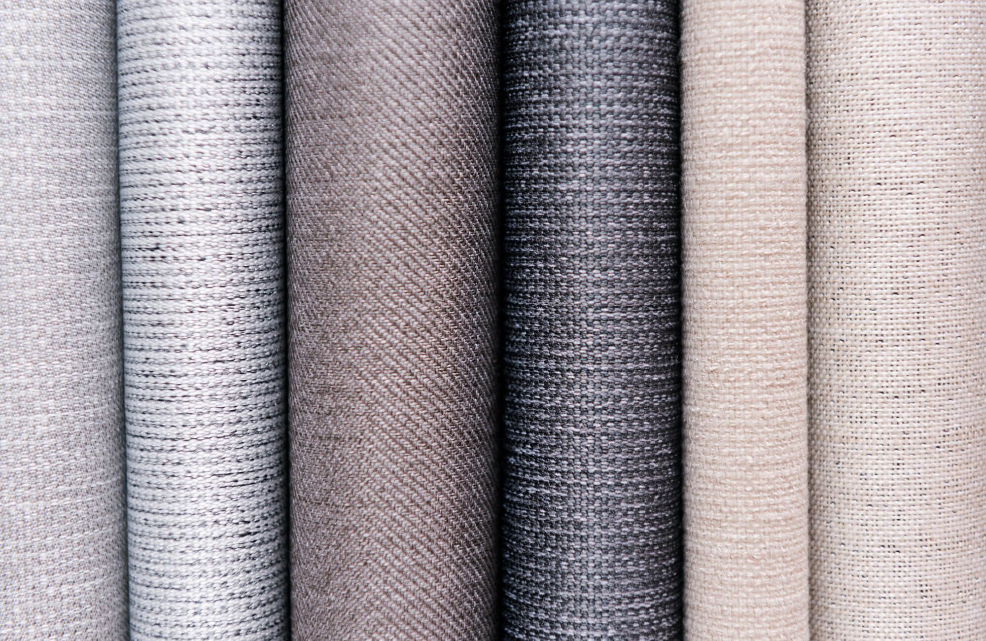 A selection of rolled fabrics in neutral tones, showcasing varied textures and weaves for a refined, sophisticated look.