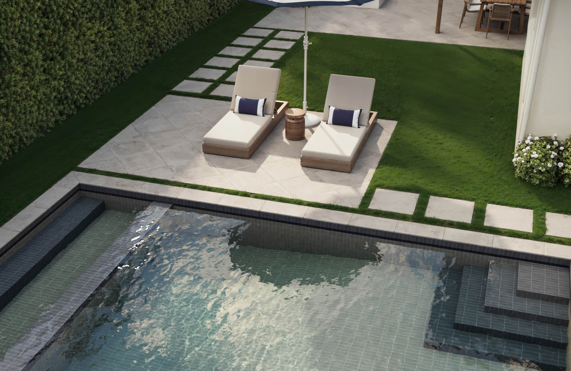 Poolside retreat with neutral-tone porcelain paver tiles, plush loungers, and vibrant green lawn accents for a crisp and upscale finish