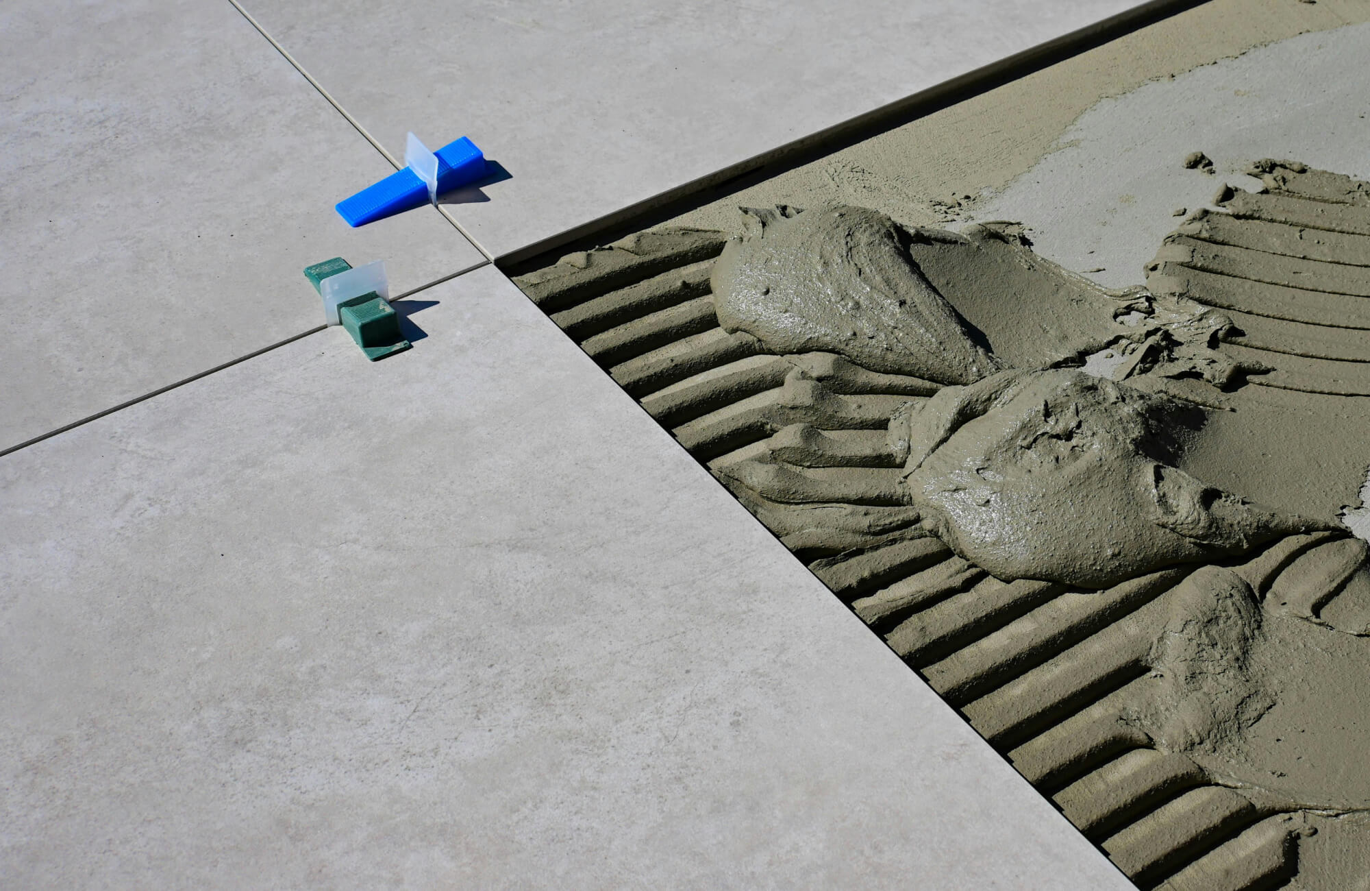 Close-up of light porcelain paver installation using thin-set mortar and leveling spacers for a durable and seamless poolside finish