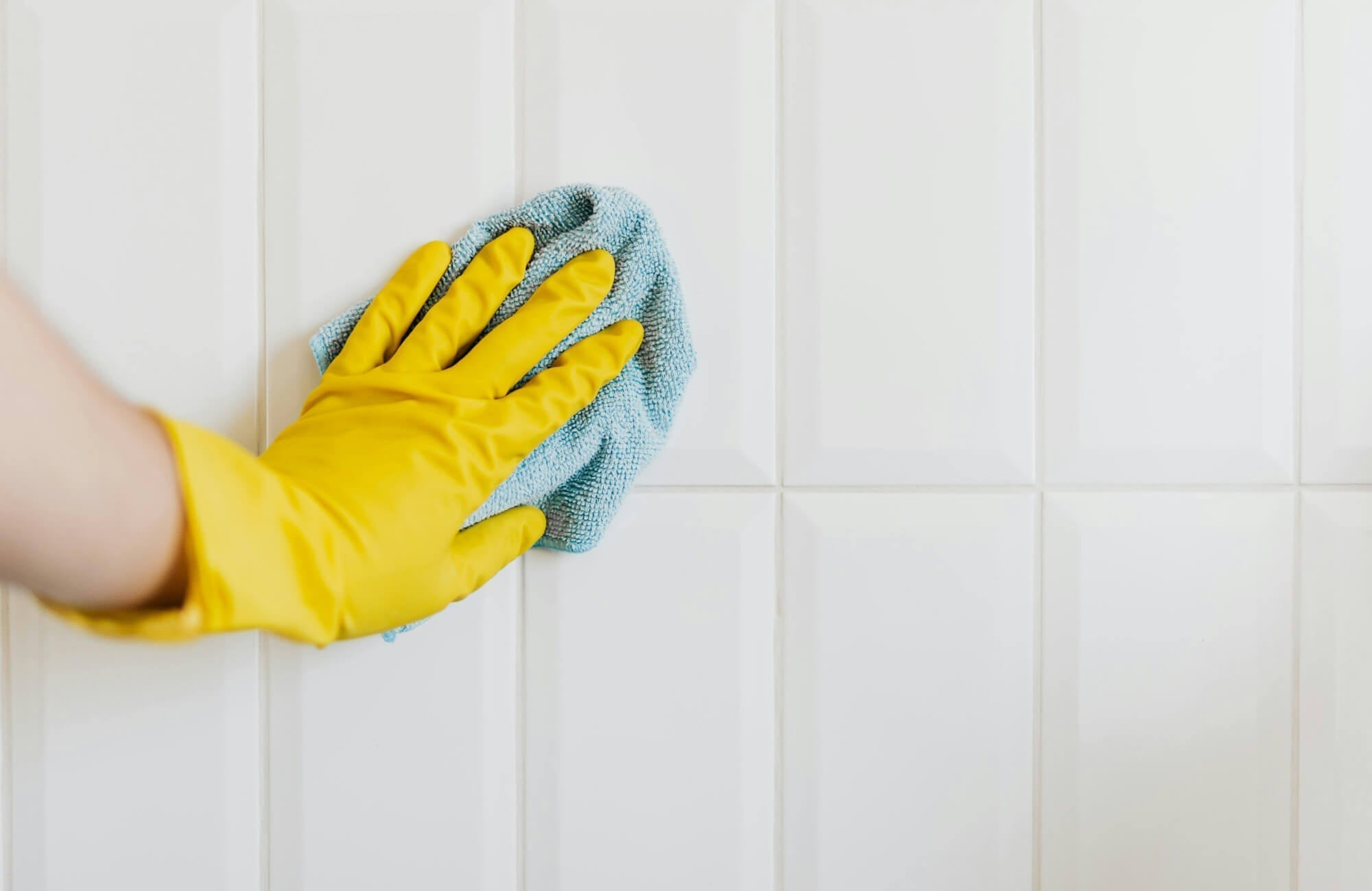 null Hand in a yellow glove, cleaning glossy white subway tiles with a blue microfiber cloth, showcasing easy maintenance and shine restoration.