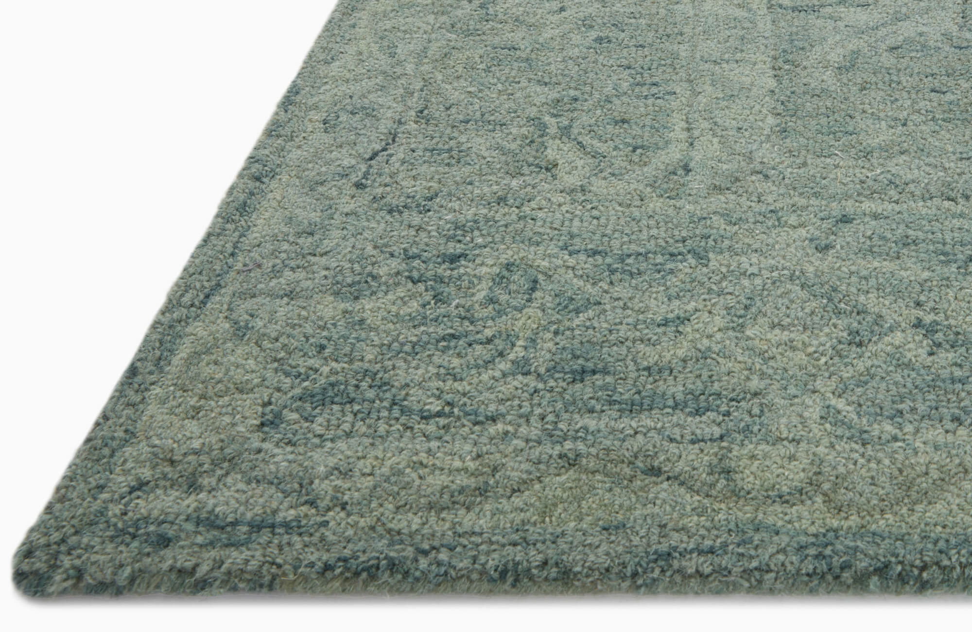 Close-up of a textured wool rug in muted teal tones, featuring a subtle looped weave and soft patterned detailing.