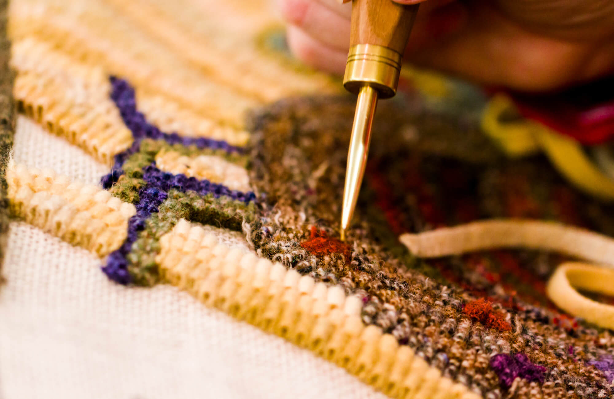 Crafting a wool rug up close, where cream and brown fibers are carefully shaped with touches of blue and red for added detail.