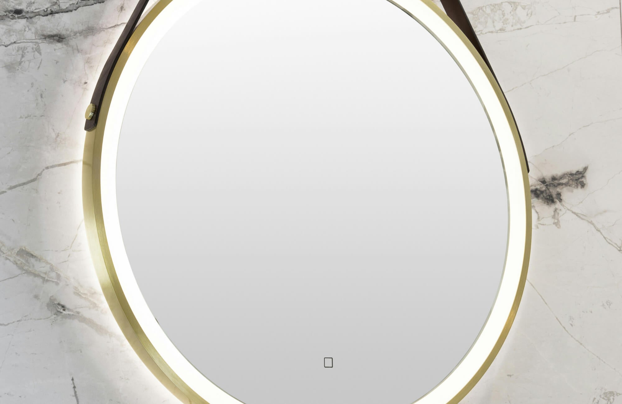 null Close-up of a round bathroom mirror with a brushed brass frame and soft LED backlighting, mounted on a white marble wall with subtle gray veining for an elegant, modern finish.