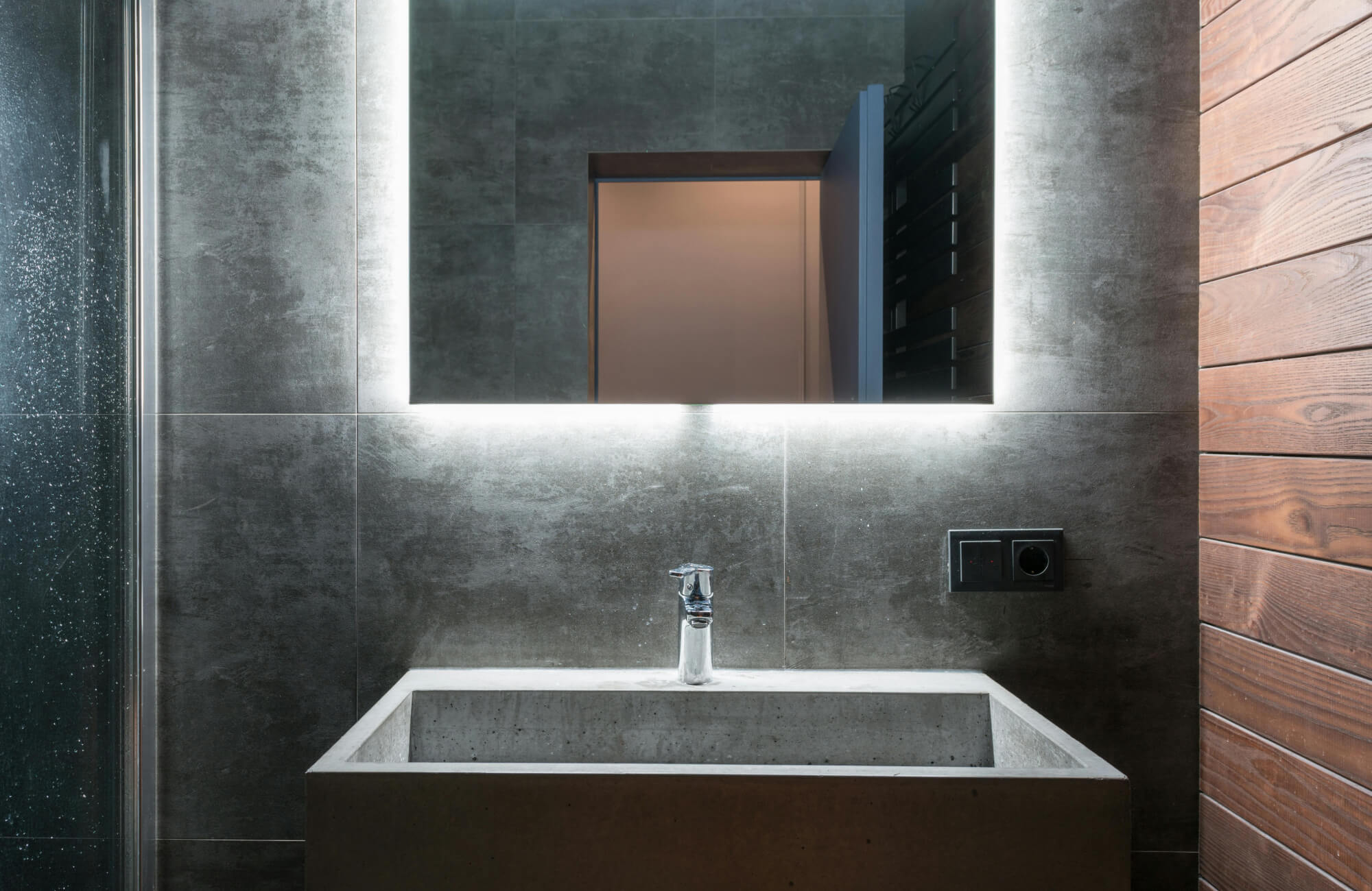 null Sleek bathroom vanity lighting with an LED backlit mirror illuminating a minimalist concrete sink and dark tiled walls for a modern, industrial aesthetic.