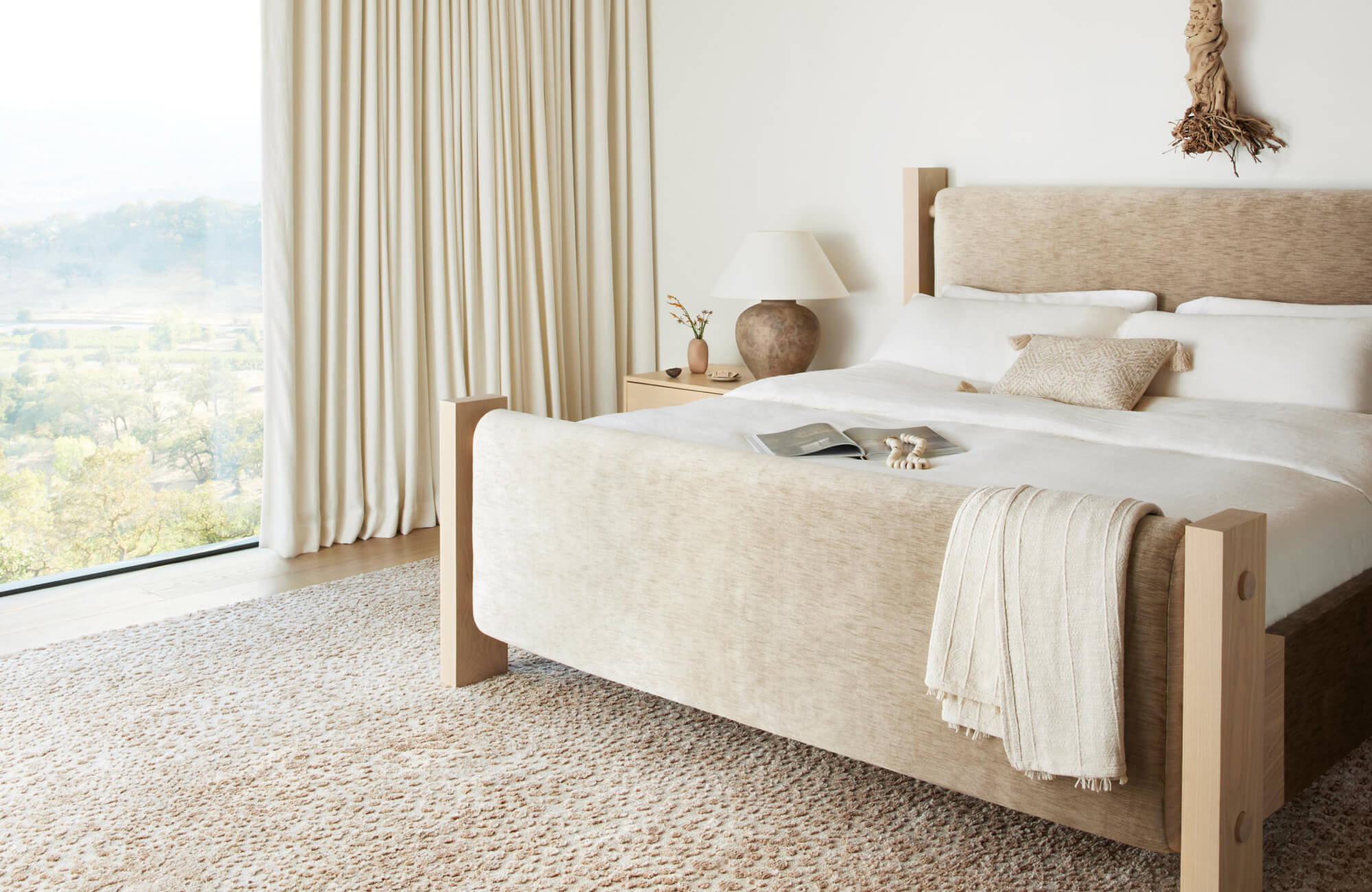Serene bedroom with a textured neutral rug grounding the space, accented by a sculptural ceramic table lamp on the nightstand that casts a soft, warm glow.