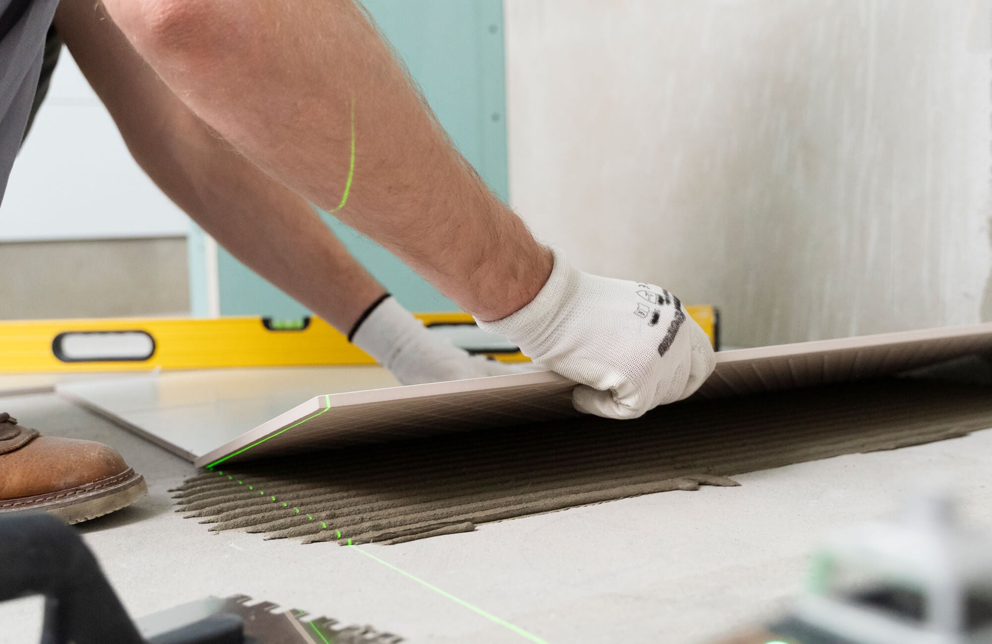 null A tile installer is placing a large-format floor tile with precision over mortar using alignment tools for proper drainage.