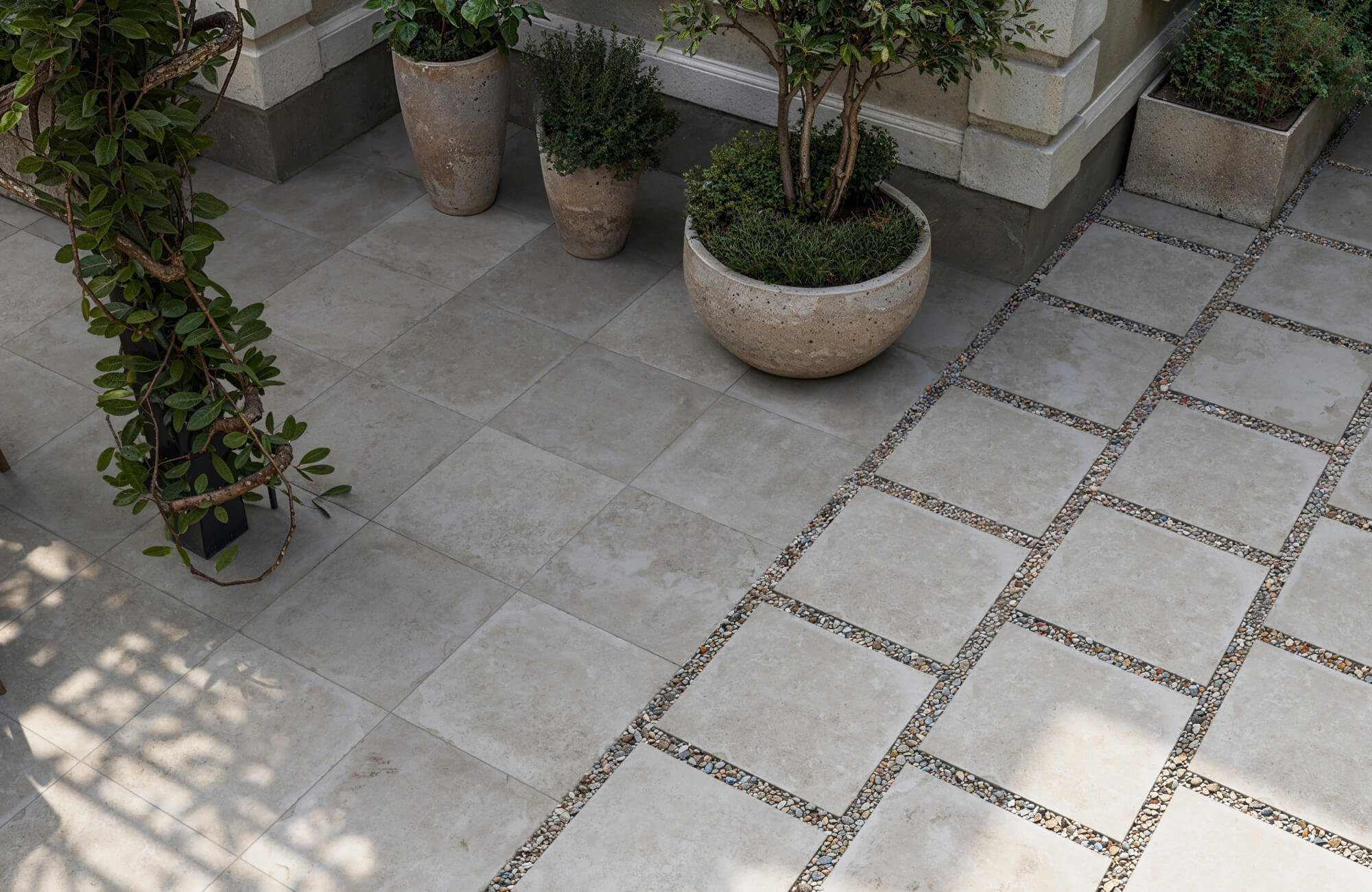 null Elegant cream-toned paver tiles laid in two styles: flush set and spaced with decorative gravel, framed by lush potted greenery.