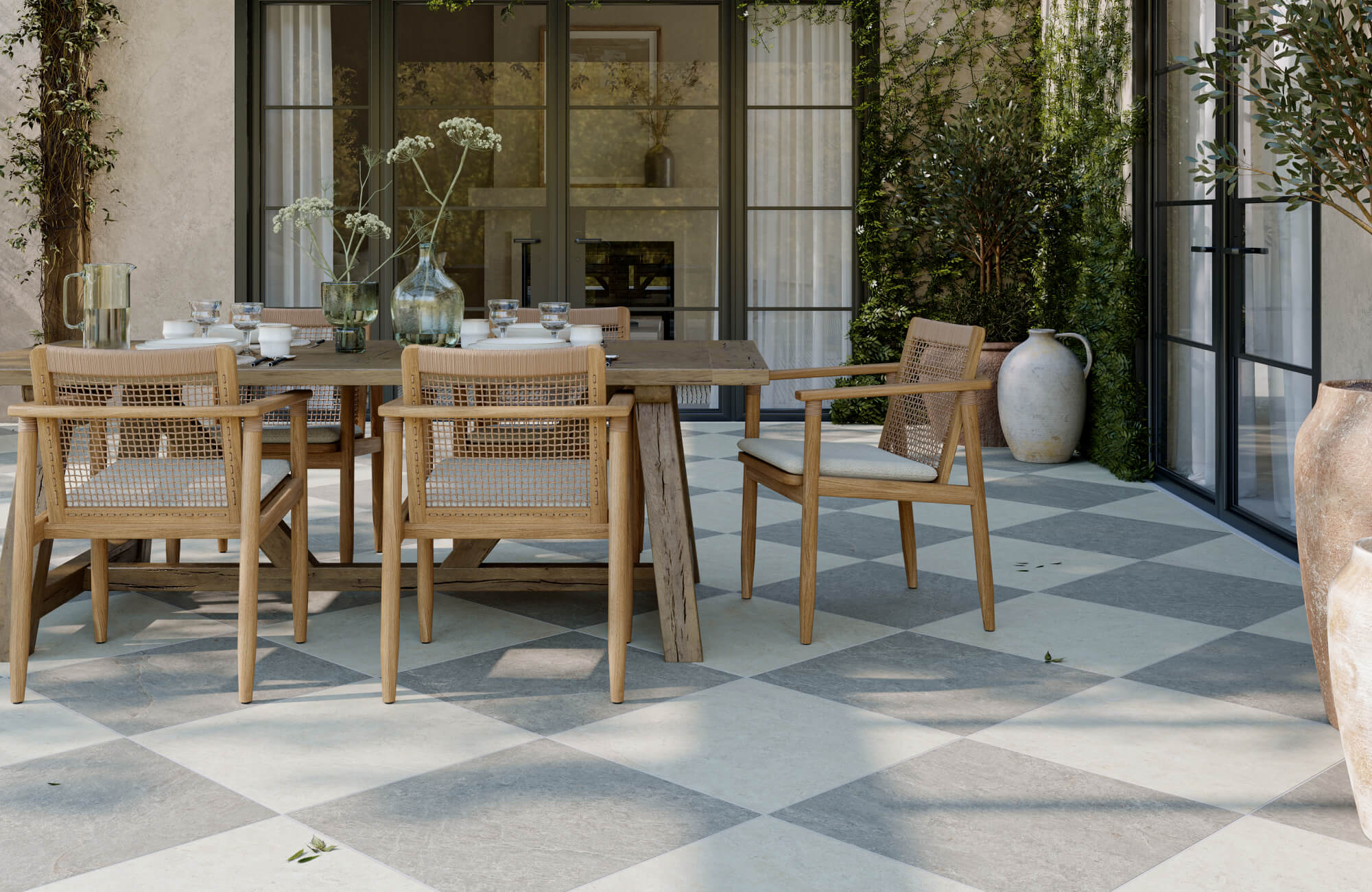 null Outdoor dining space with checkered porcelain paver tiles in soft gray and cream tones, paired with light wood furniture and lush greenery