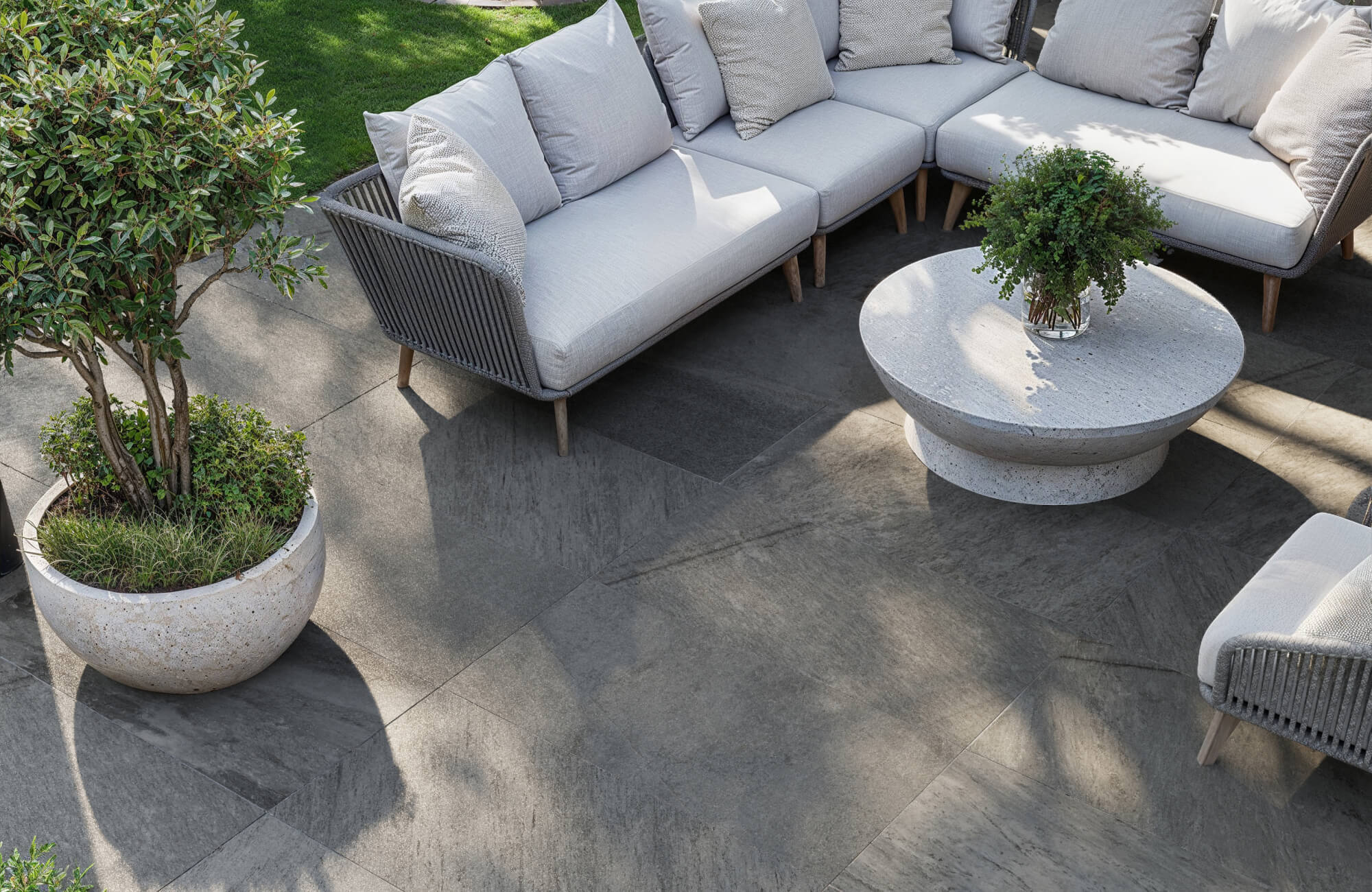 null Modern outdoor lounge with charcoal-toned porcelain paver tiles, plush light-gray sectional seating, and a sculptural round stone table