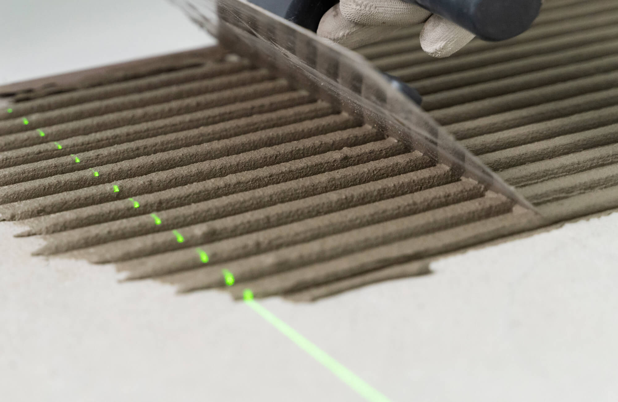 Close-up of a trowel spreading thin-set mortar in even ridges along a laser guide line, preparing the surface for subway tile installation.